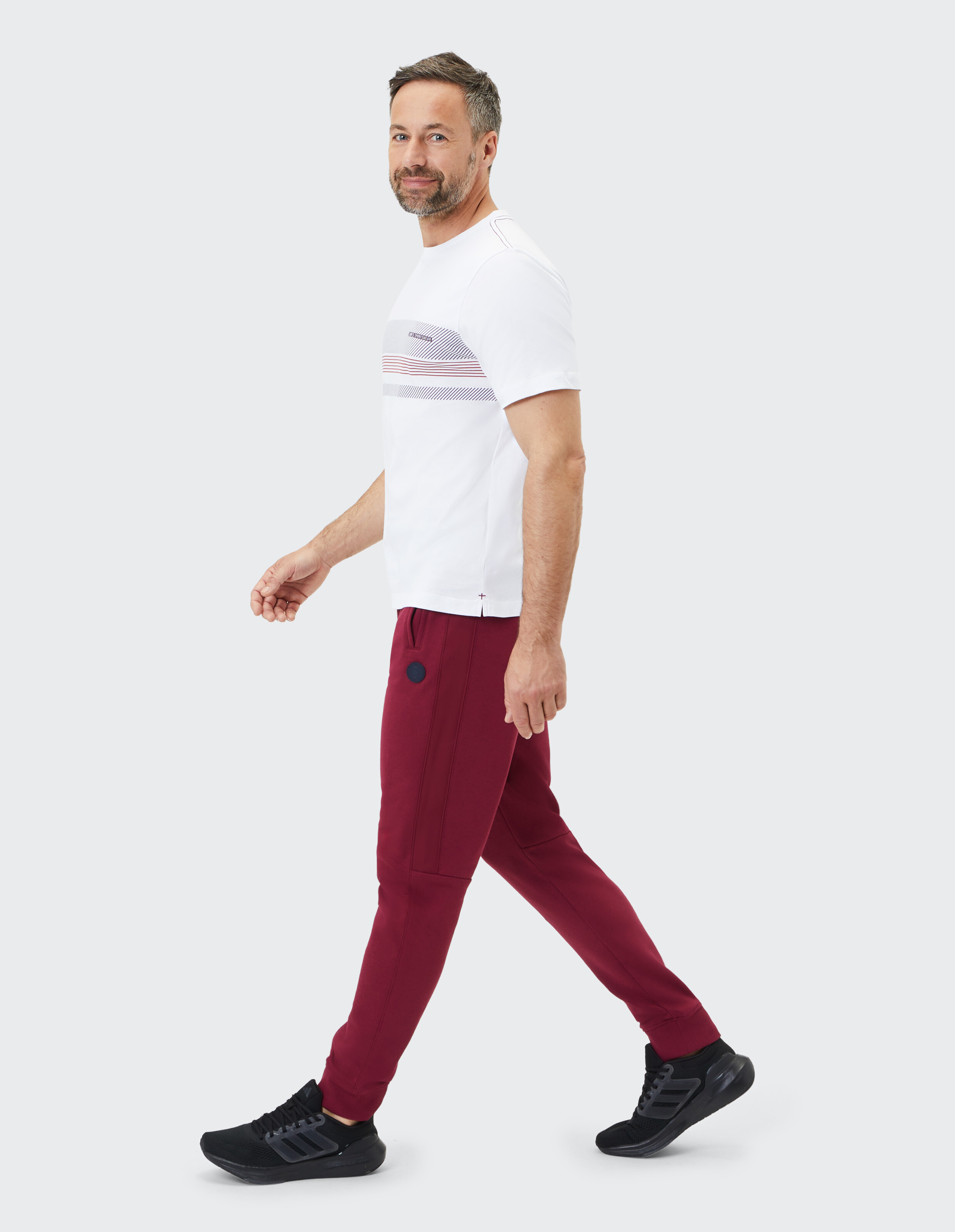 Mann in weißem T-Shirt und burgunderfarbenen Jogginghosen geht lässig und stilvoll bequem spazieren.