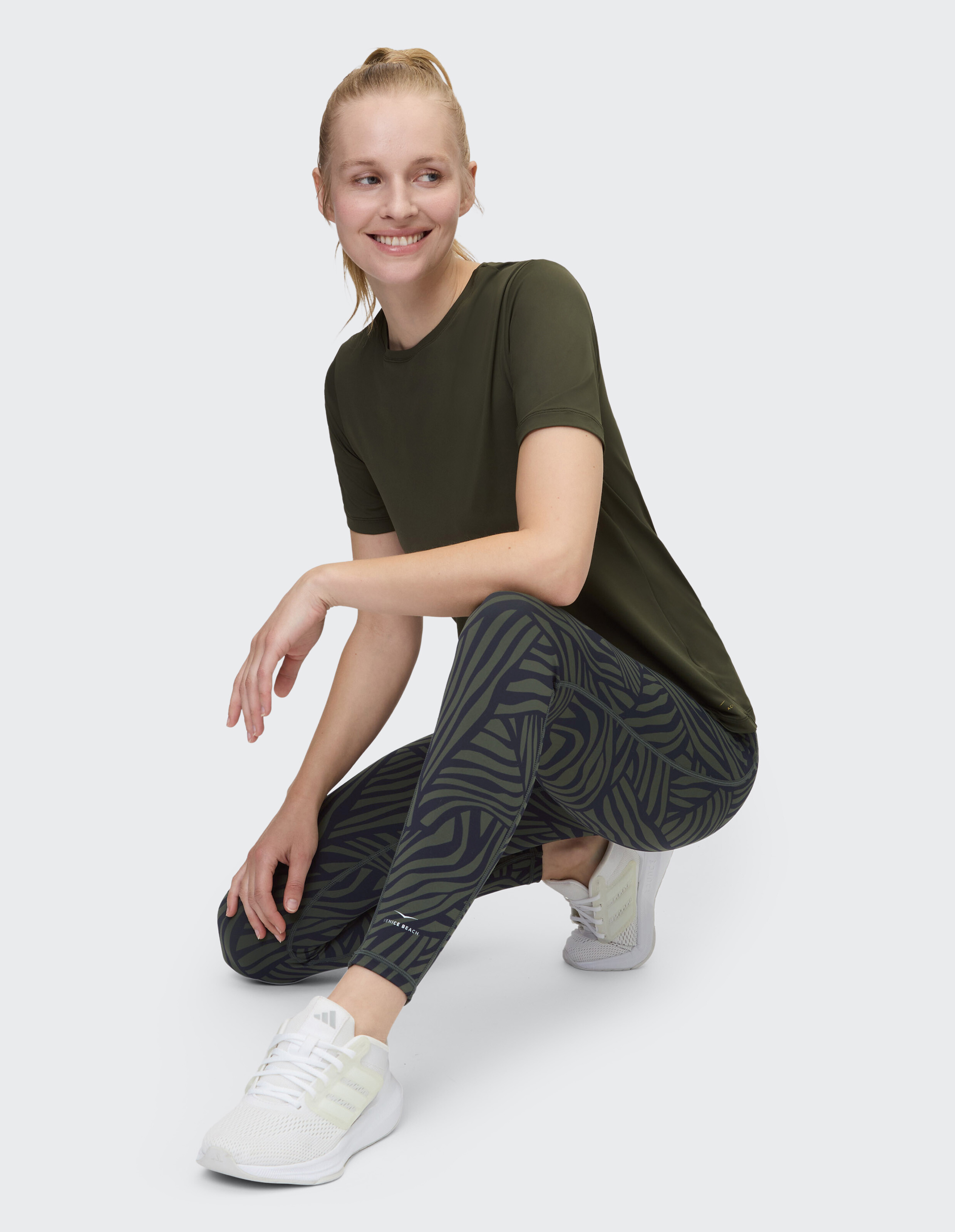 Frau in olivgrünem T-Shirt und gemusterten Leggings, gestylt für lässigen Komfort.