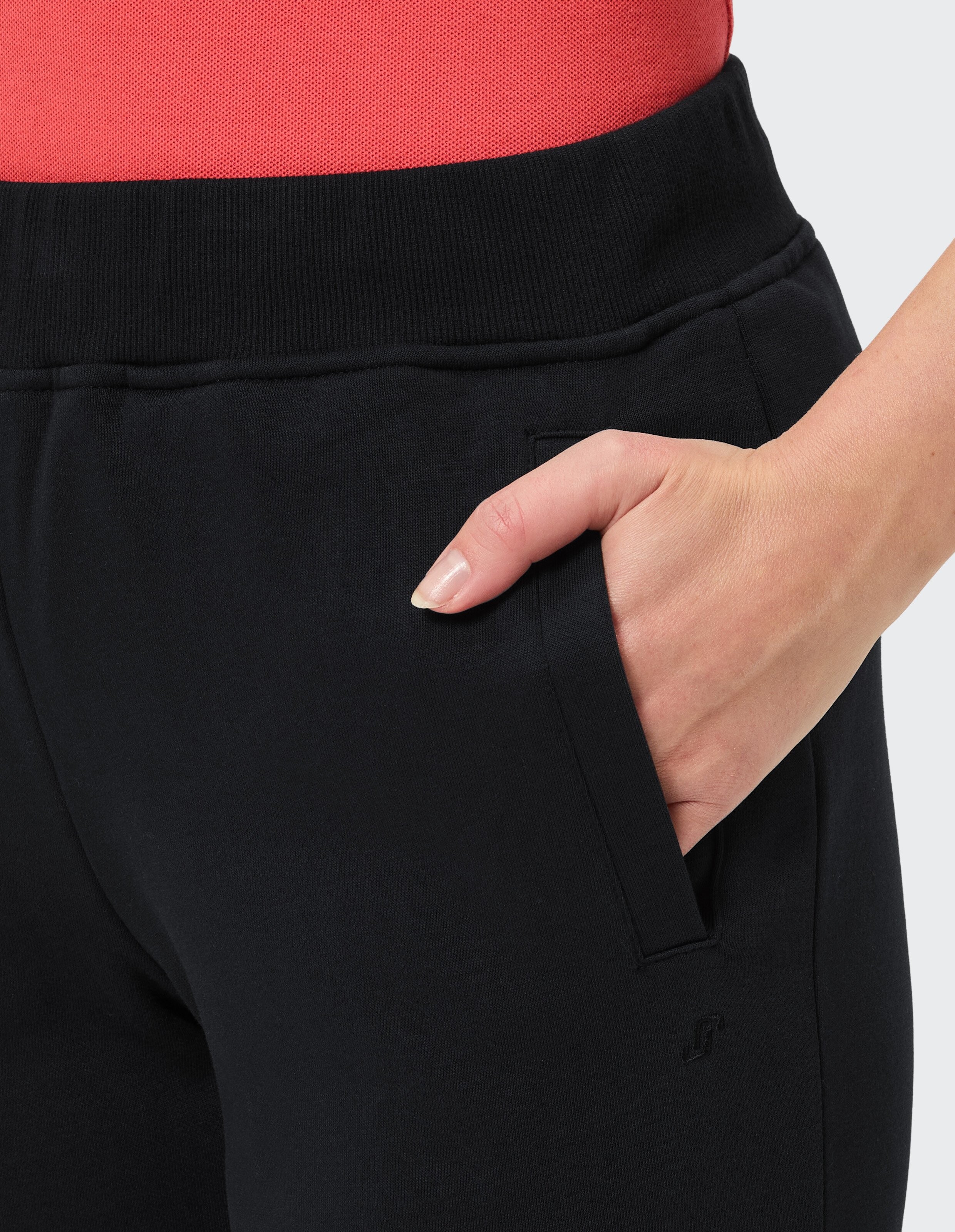 Nahaufnahme einer Hand, die in der Hosentasche einer schwarzen Hose steckt, getragen mit einem rosa-weiß gestreiften Oberteil.