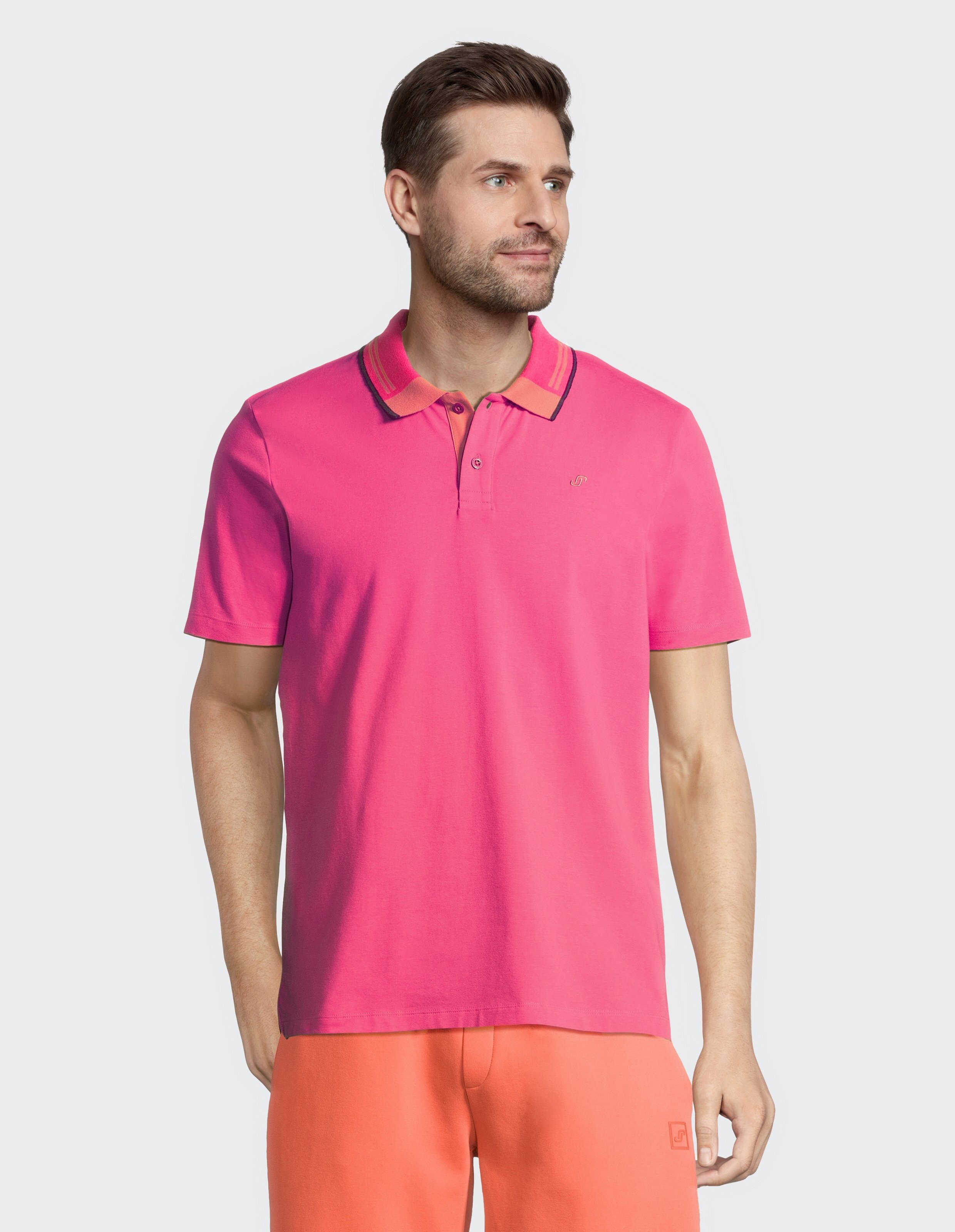 Mann trägt ein leuchtend rosa Poloshirt mit gestreiftem Kragen, perfekt für den lässigen Sommerstil.