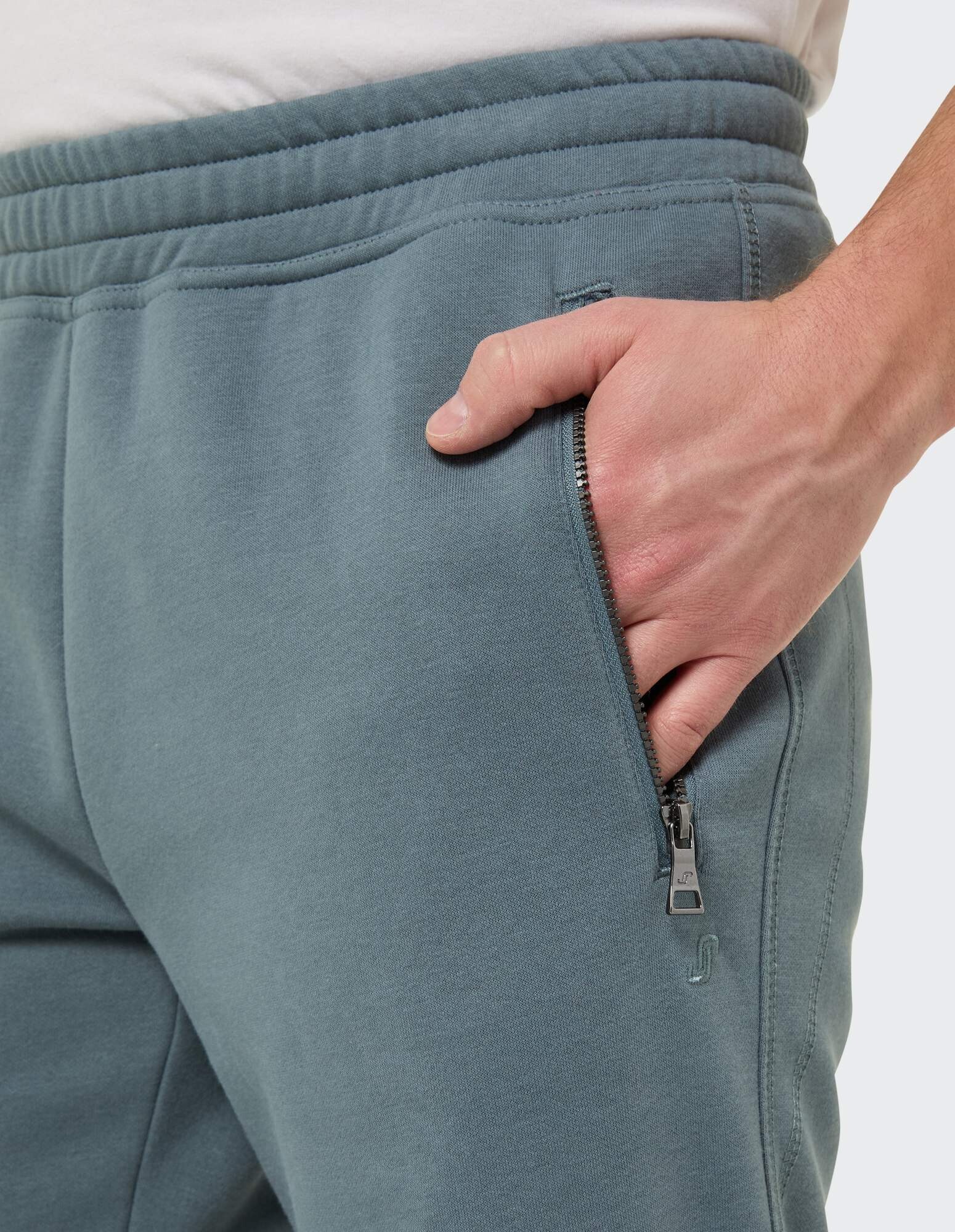 Nahaufnahme einer blaugrünen Jogginghose mit Reißverschlusstasche, perfekt für Freizeitkleidung.