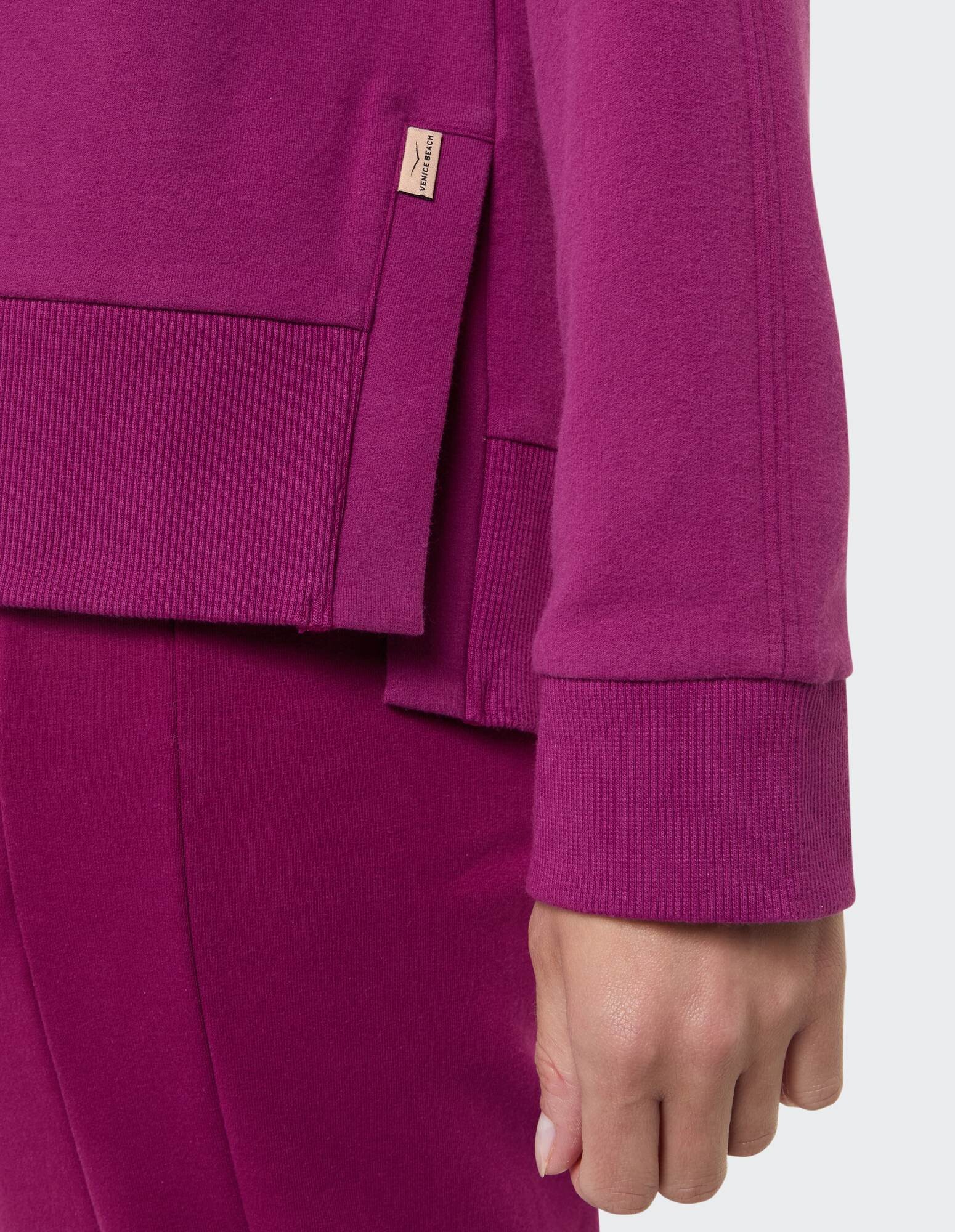 Nahaufnahme eines kuscheligen lila Sweatshirts mit gerippten Bündchen und stilvollen Details.