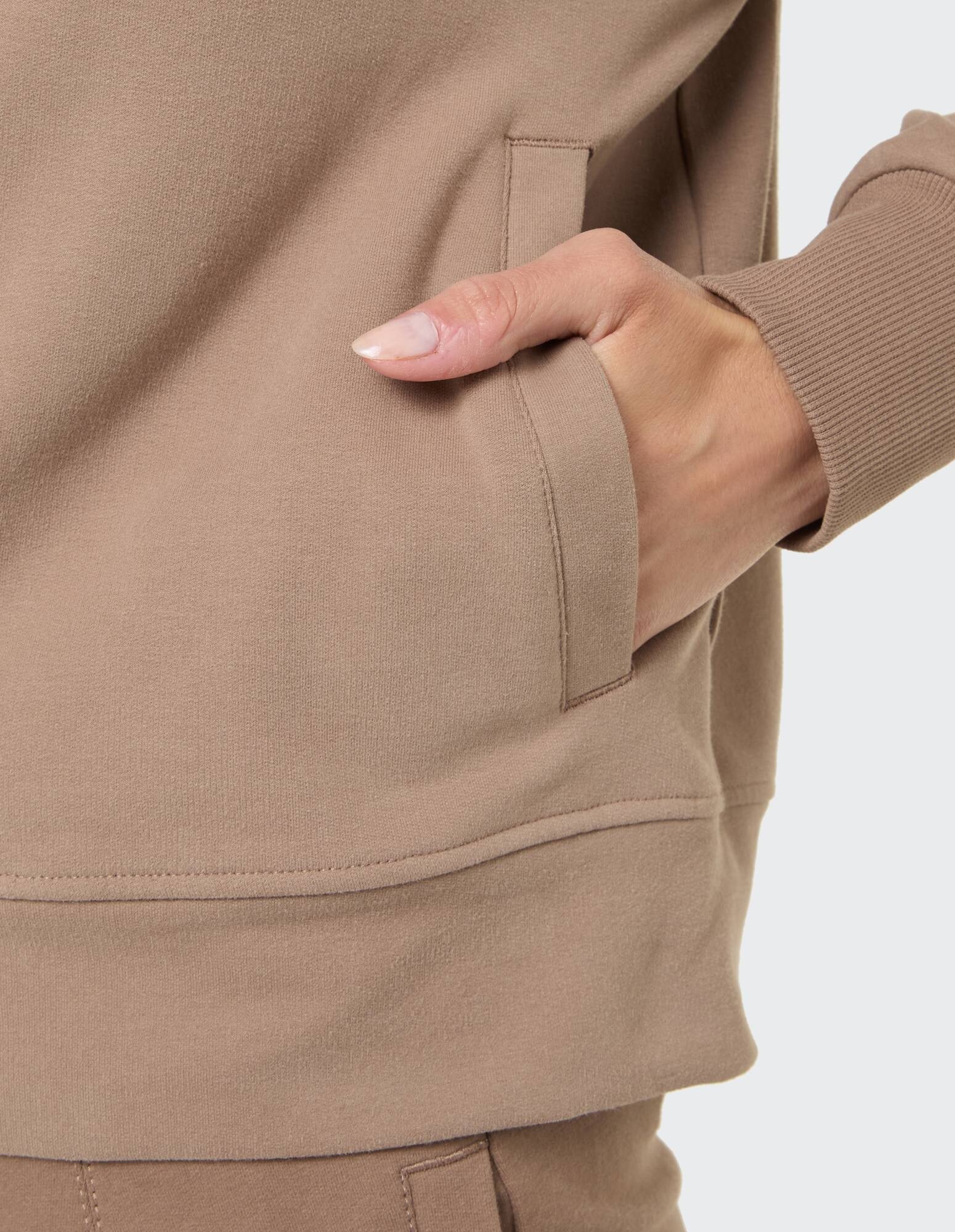 Nahaufnahme eines kuscheligen beigen Sweatshirts mit Seitentasche und gerippten Bündchen.