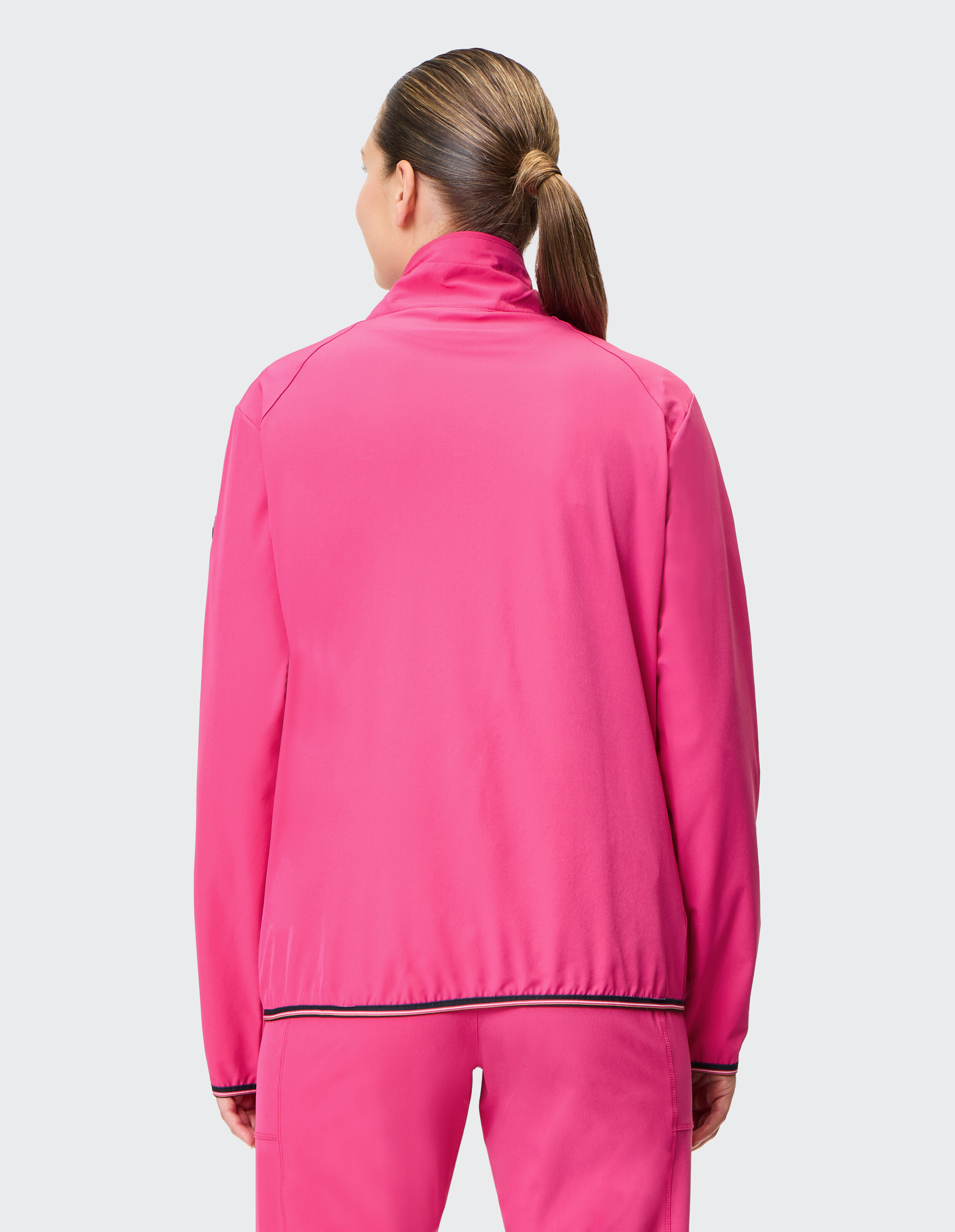 Rückansicht einer Frau, die zum Faulenzen eine leuchtend rosafarbene Freizeitjacke mit Reißverschluss trägt.