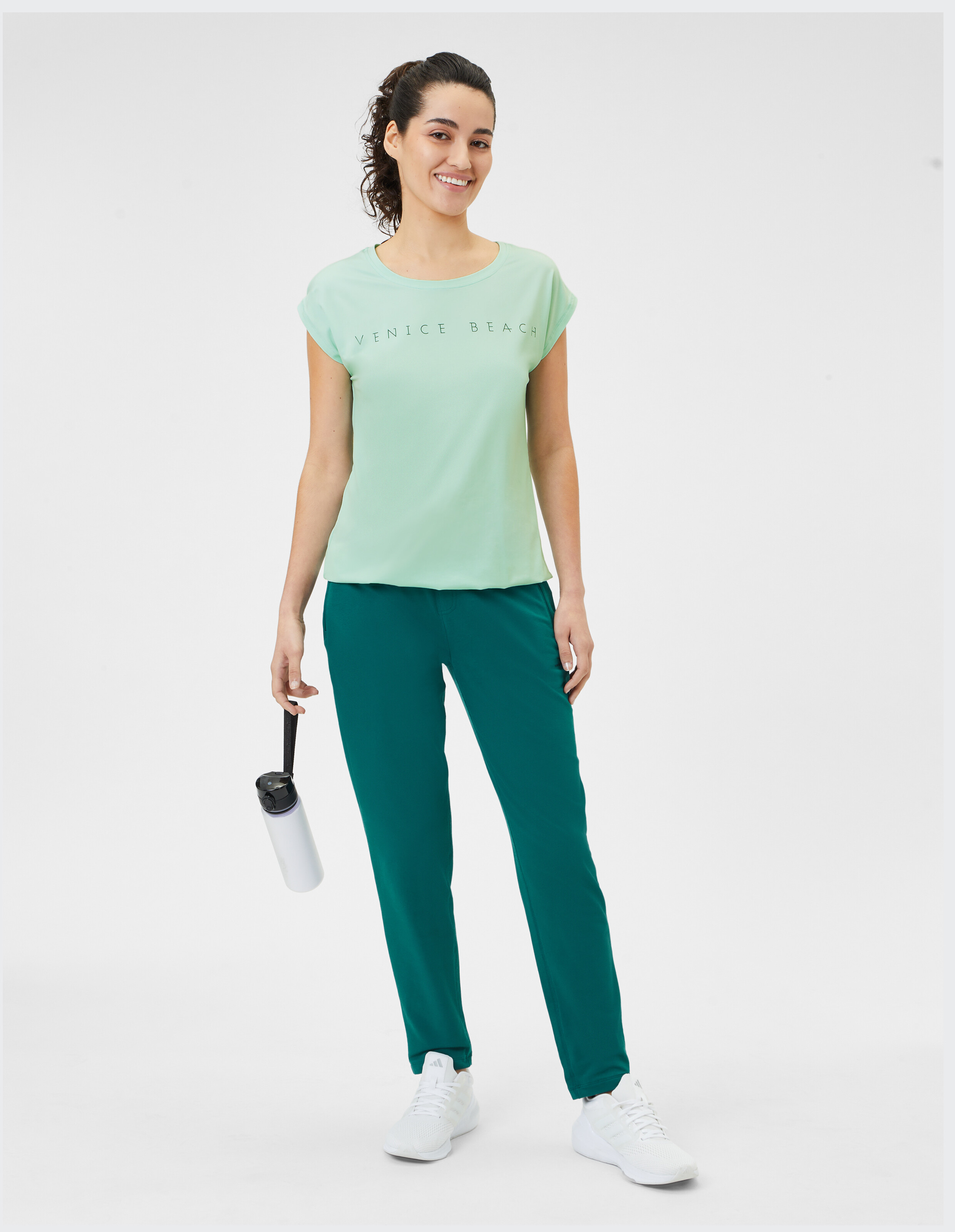 Frau in einem hellgrünen Venice Beach-T-Shirt und einer dunkelgrünen Freizeithose.