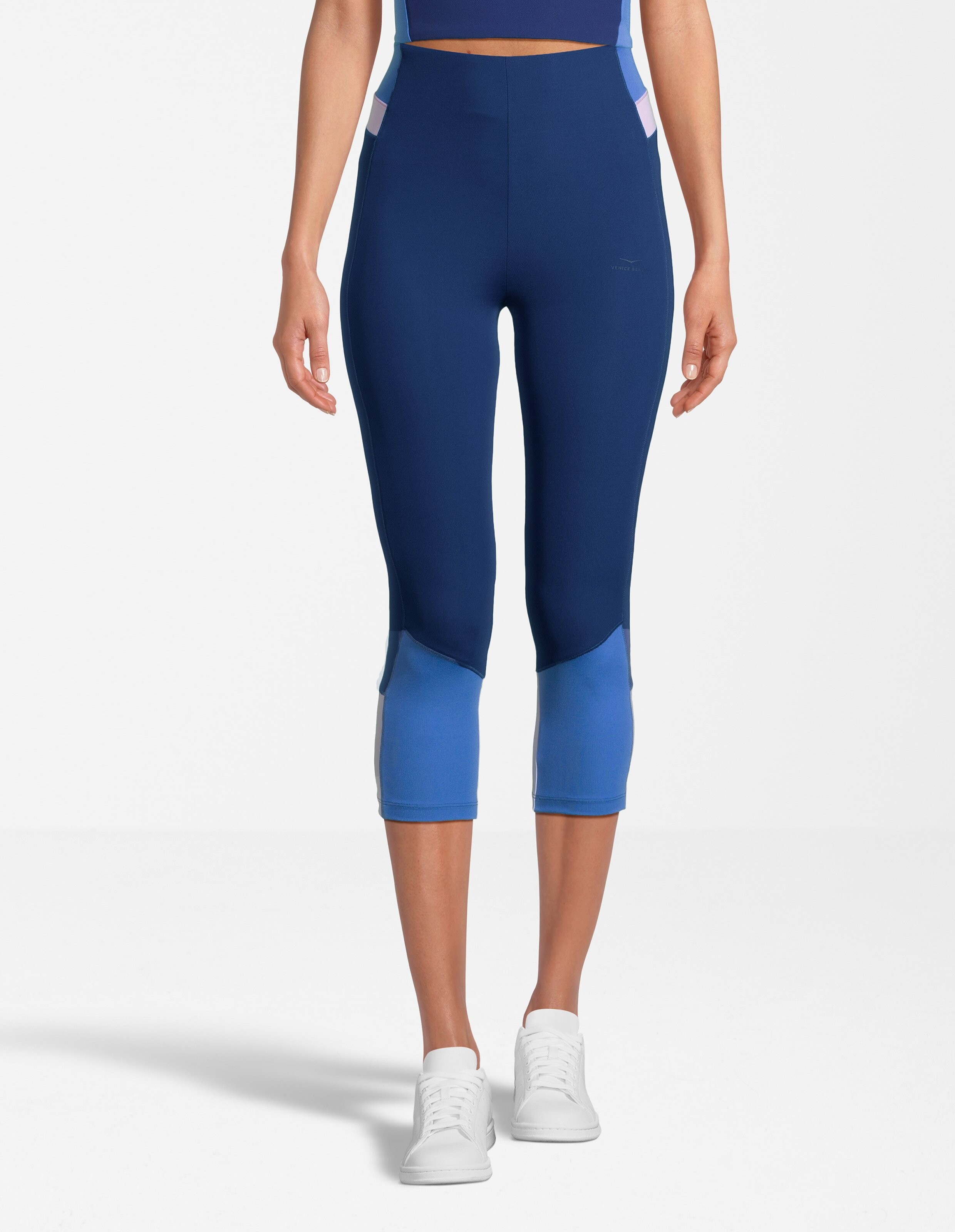 Frau trägt blaue, kurz geschnittene Leggings in Colour-Block-Optik für lässigen Athleisure-Stil.