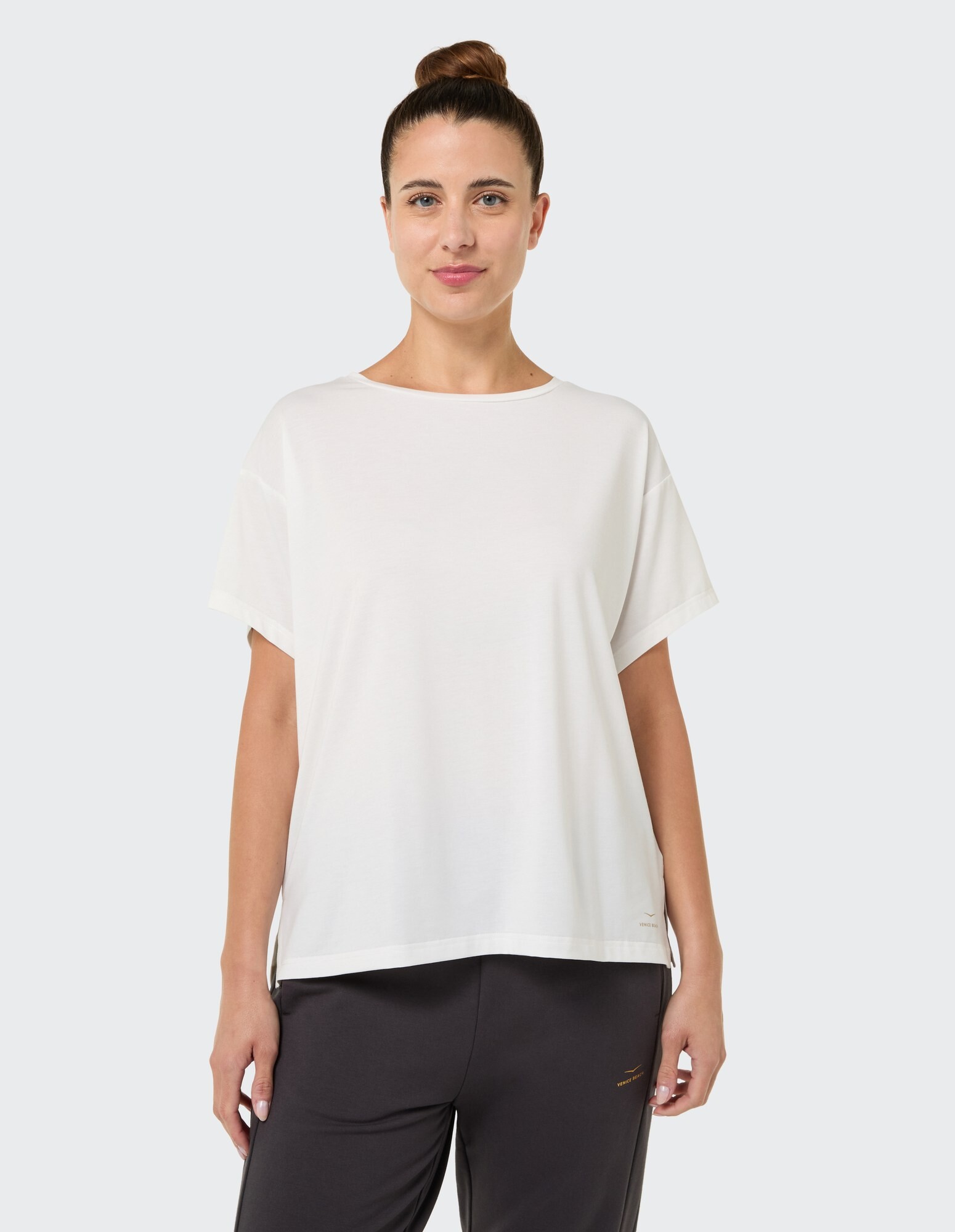 Frau in einem weißen, lässigen T-Shirt, gepaart mit einer dunklen Hose, zeigt einen entspannten Stil.