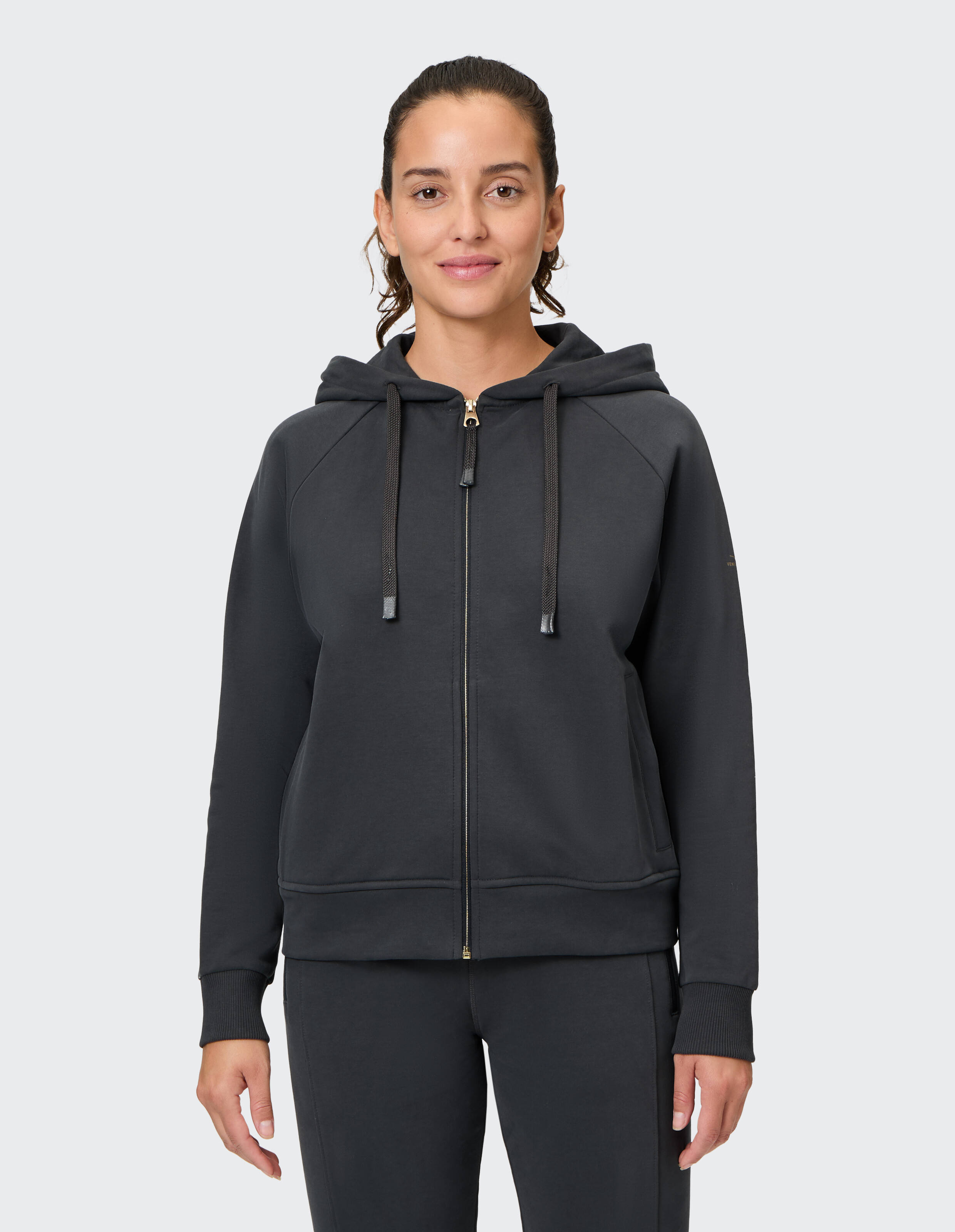 Frau trägt einen kuscheligen schwarzen Kapuzenpullover mit Reißverschluss, Kapuze und Kordelzug für lässige Loungewear.
