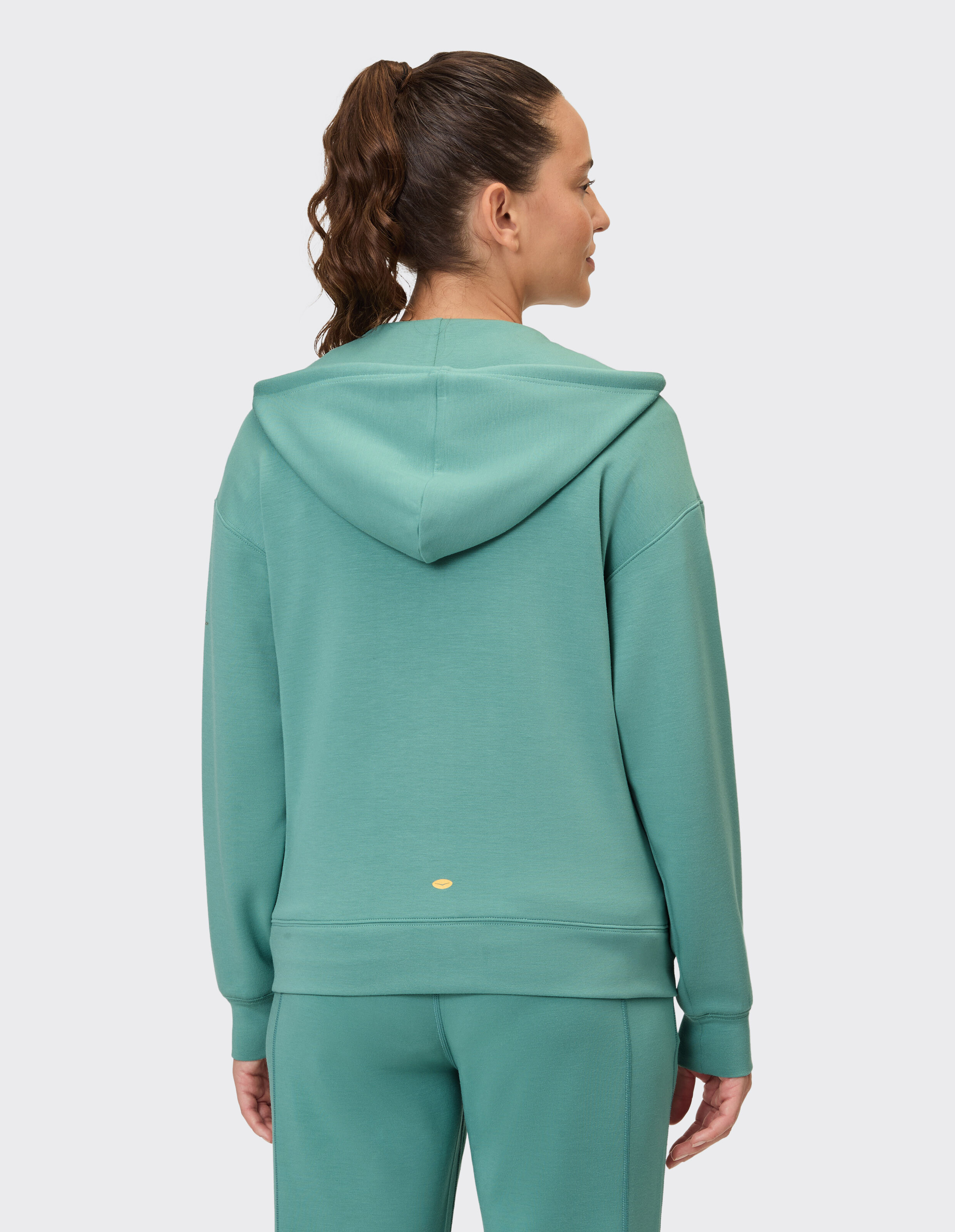 Frau trägt einen gemütlichen salbeigrünen Kapuzenpullover mit Reißverschluss, perfekt für lässige Loungewear.