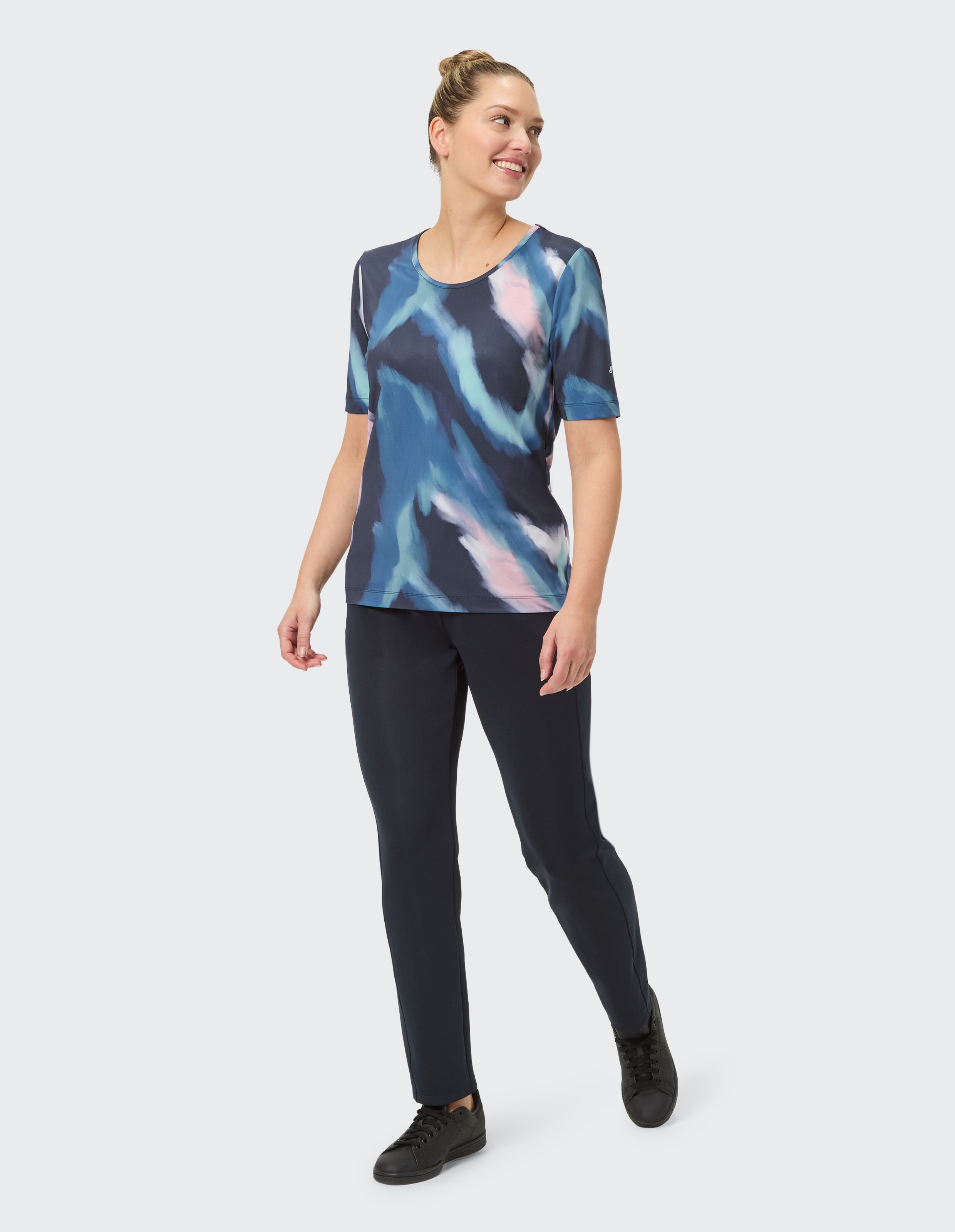 Frau trägt ein JOY Sportswear Kurzarmshirt Avena mit blauem abstraktem Print.