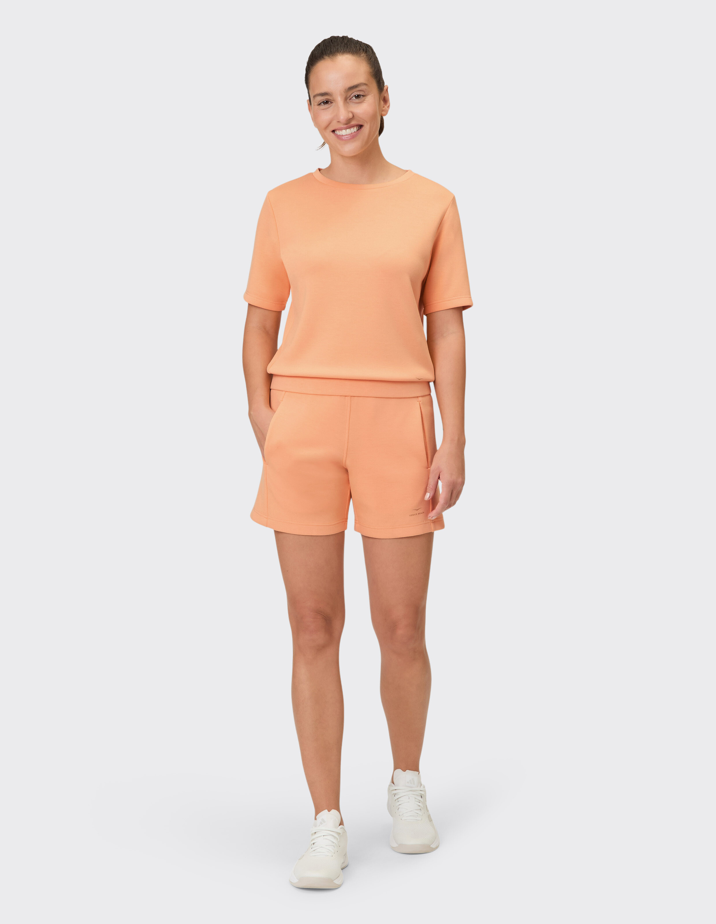 Frau trägt ein gemütliches pfirsichfarbenes Freizeit-T-Shirt und passende Shorts.