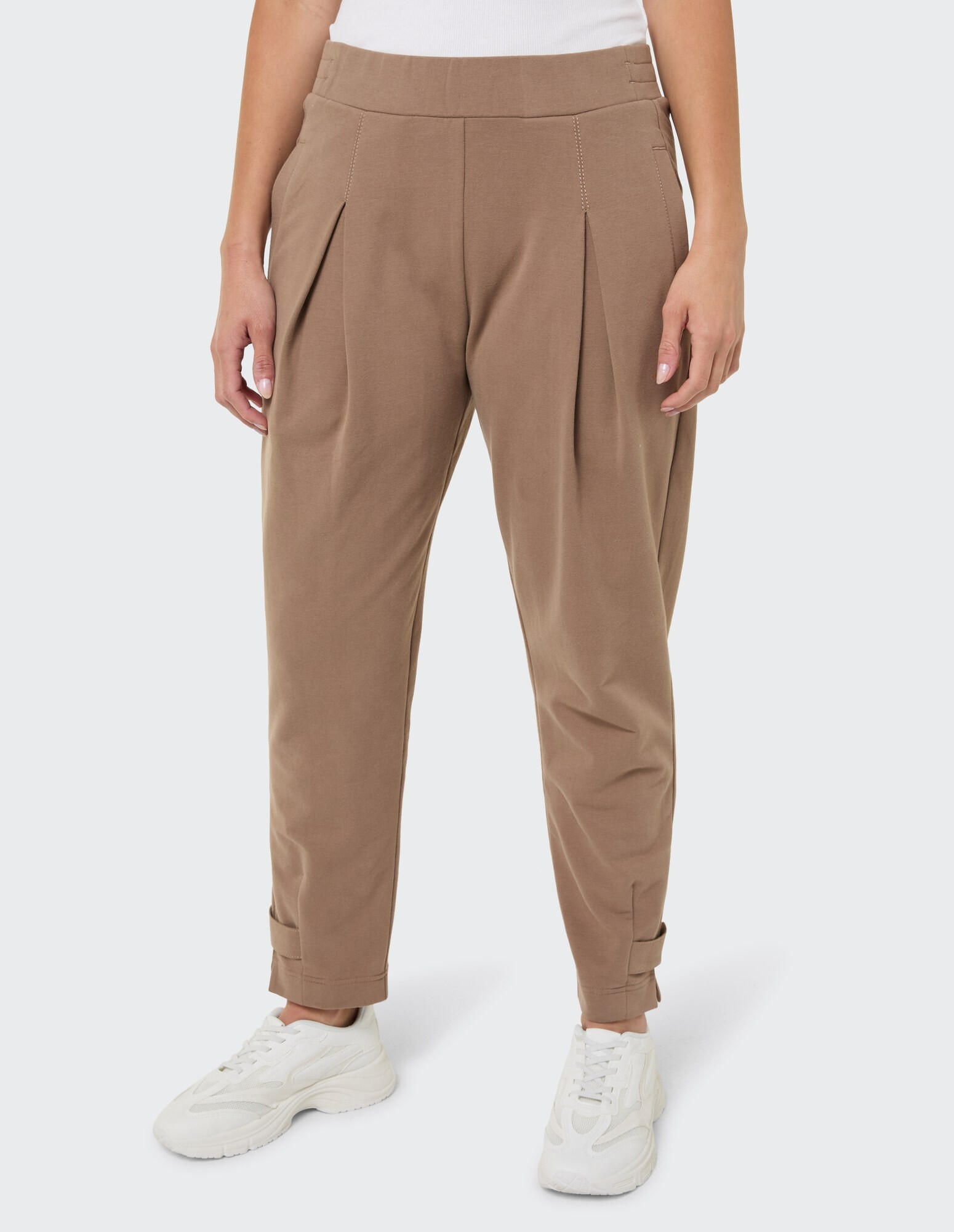 Lässige braune Bundfaltenhose mit Bündchen am Saum, gepaart mit weißen Sneakers.