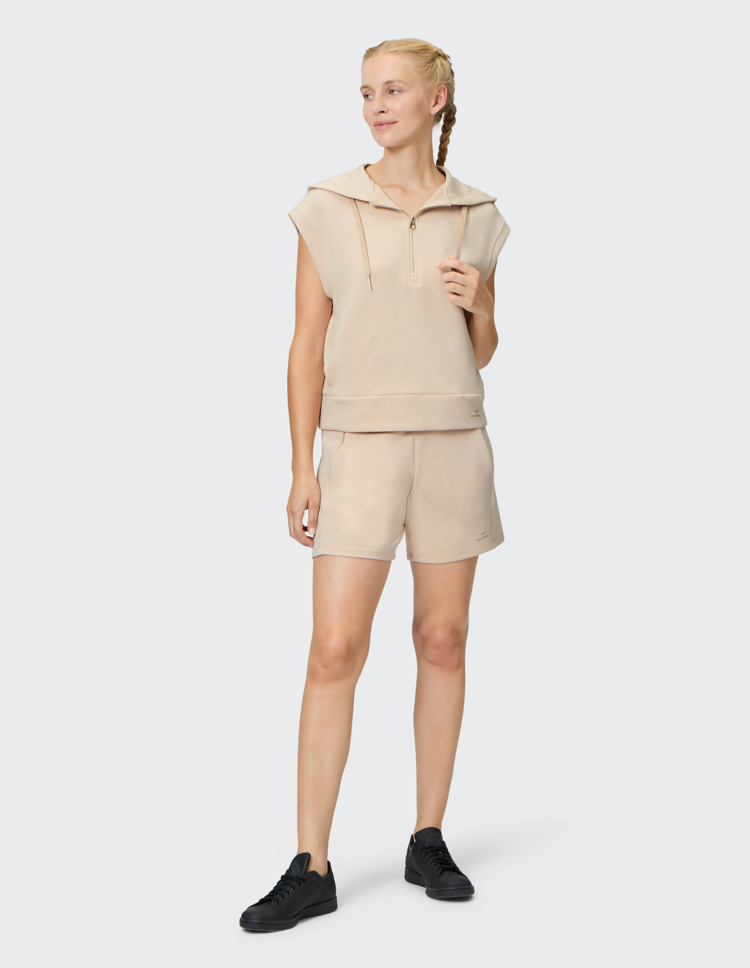 Frau trägt einen beigen ärmellosen Hoodie von Venice Beach und passende Shorts.