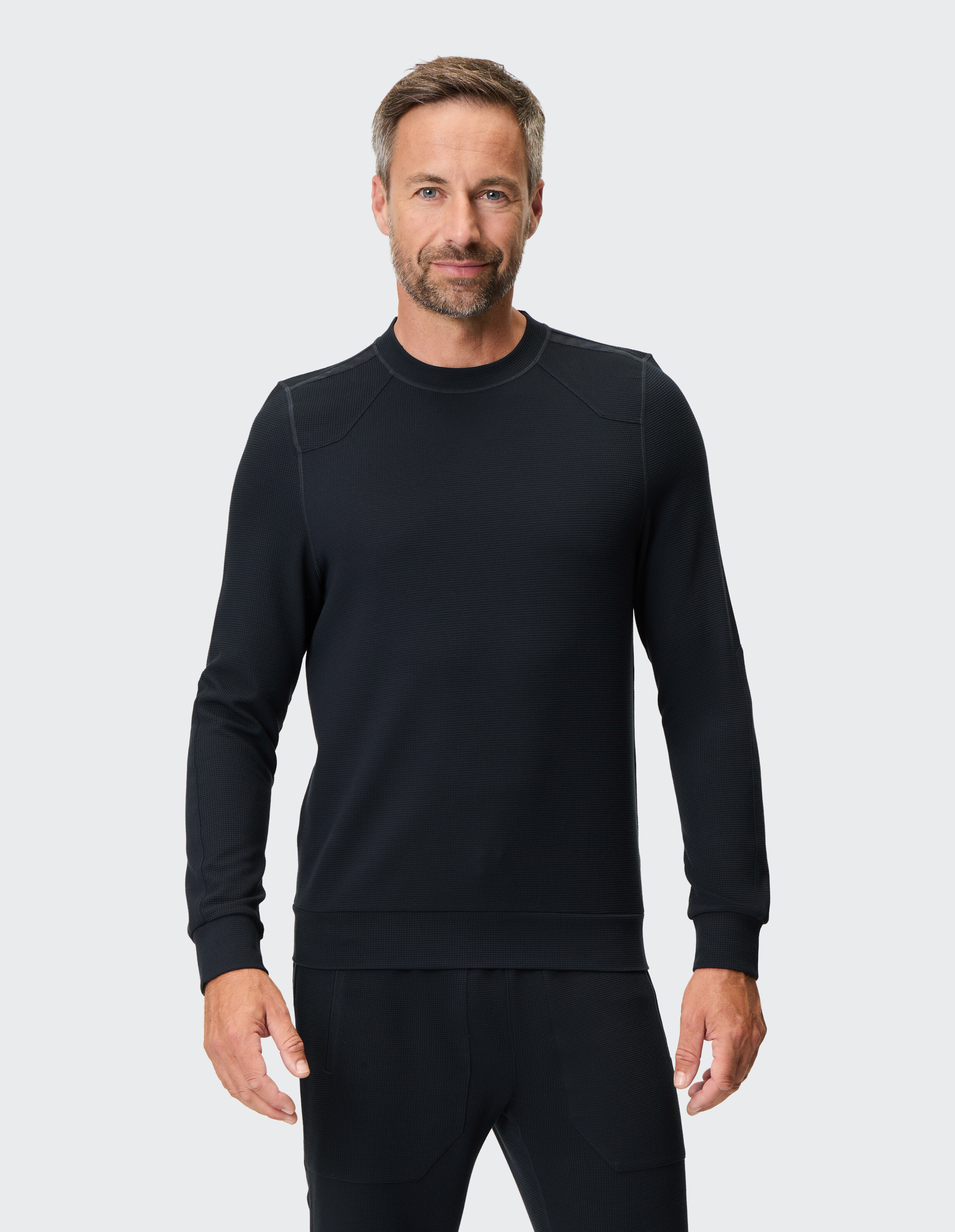 Mann trägt einen schwarzen langärmeligen Waffelstrickpullover für einen gemütlichen, lässigen Stil.