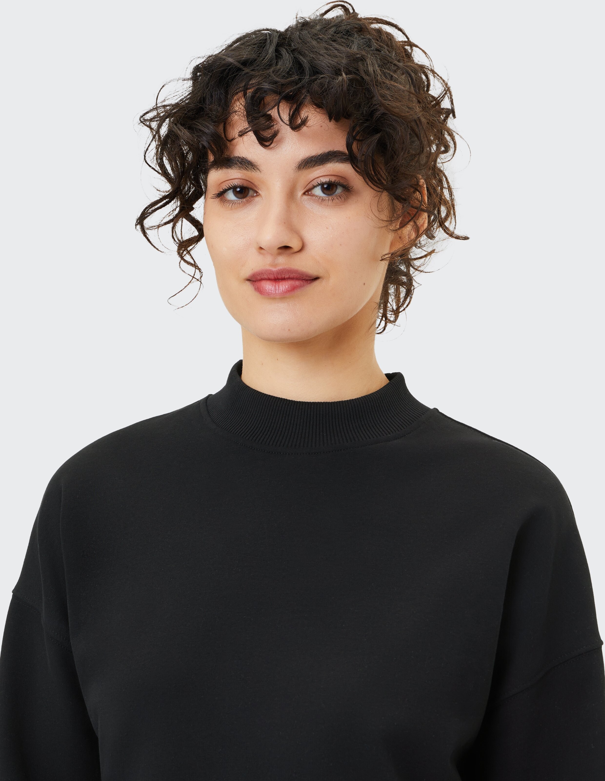 Nahaufnahme einer Frau in einem schwarzen Sweatshirt mit hohem Kragen, die einen lässigen Stil unterstreicht.