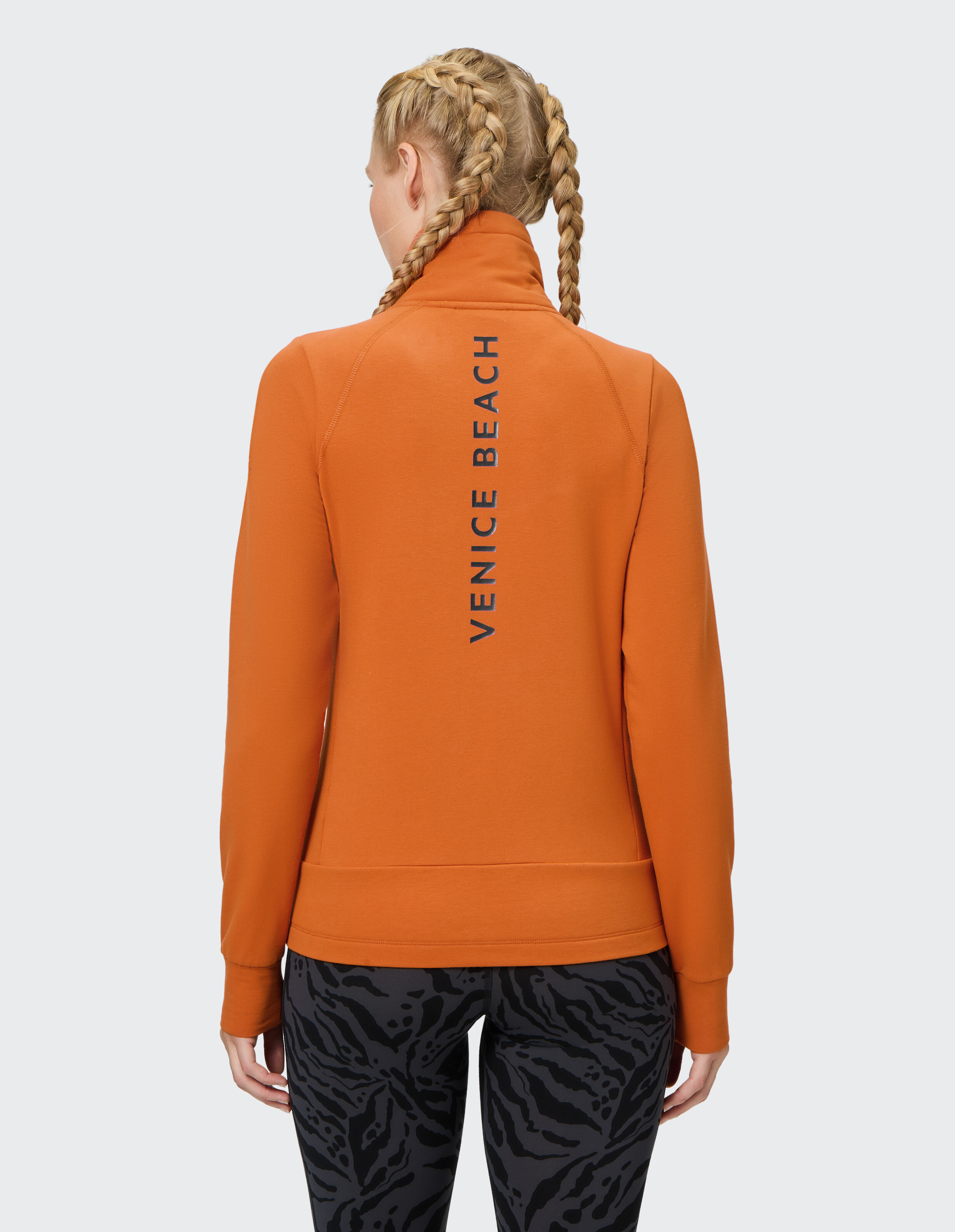 Rückansicht einer Frau in einer orangefarbenen Reißverschlussjacke mit dem Text „Venice Beach“.