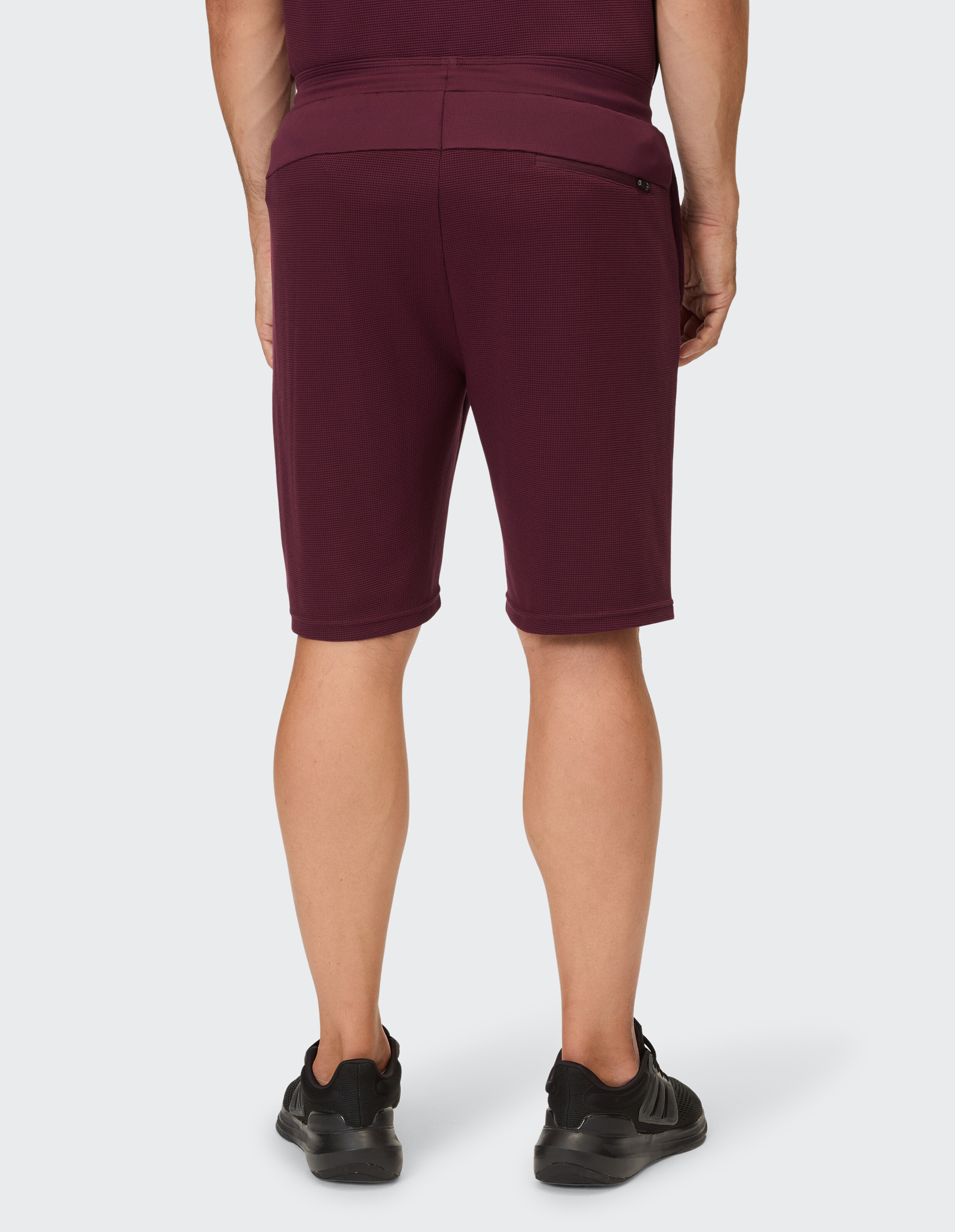 Eine Person trägt burgunderfarbene Shorts mit einem Waffel-Muster und schwarzen Turnschuhen.