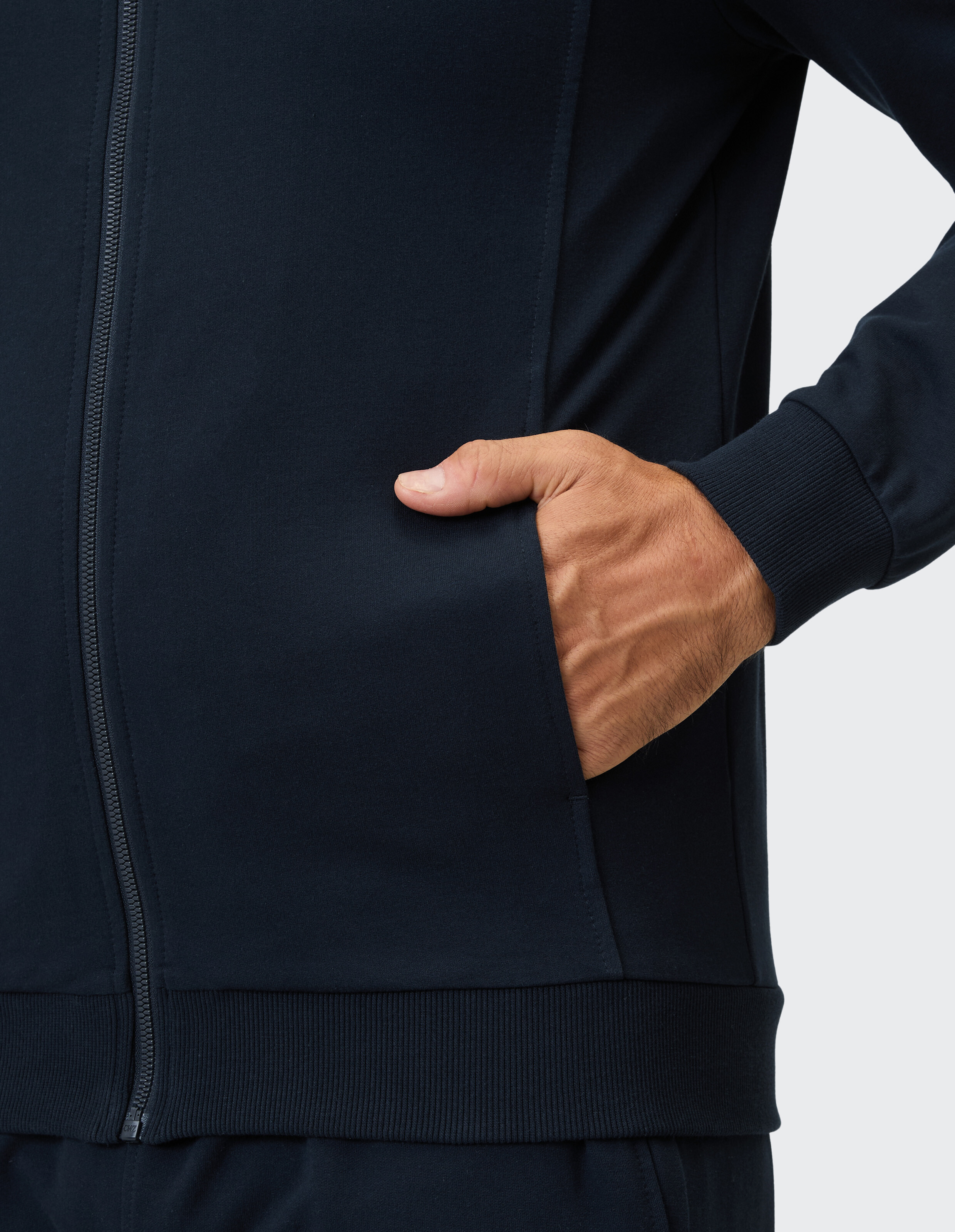 Eine dunkelblaue Kapuzenjacke mit Reißverschluss und einer integrierten Tasche wird von einer Hand benutzt.
