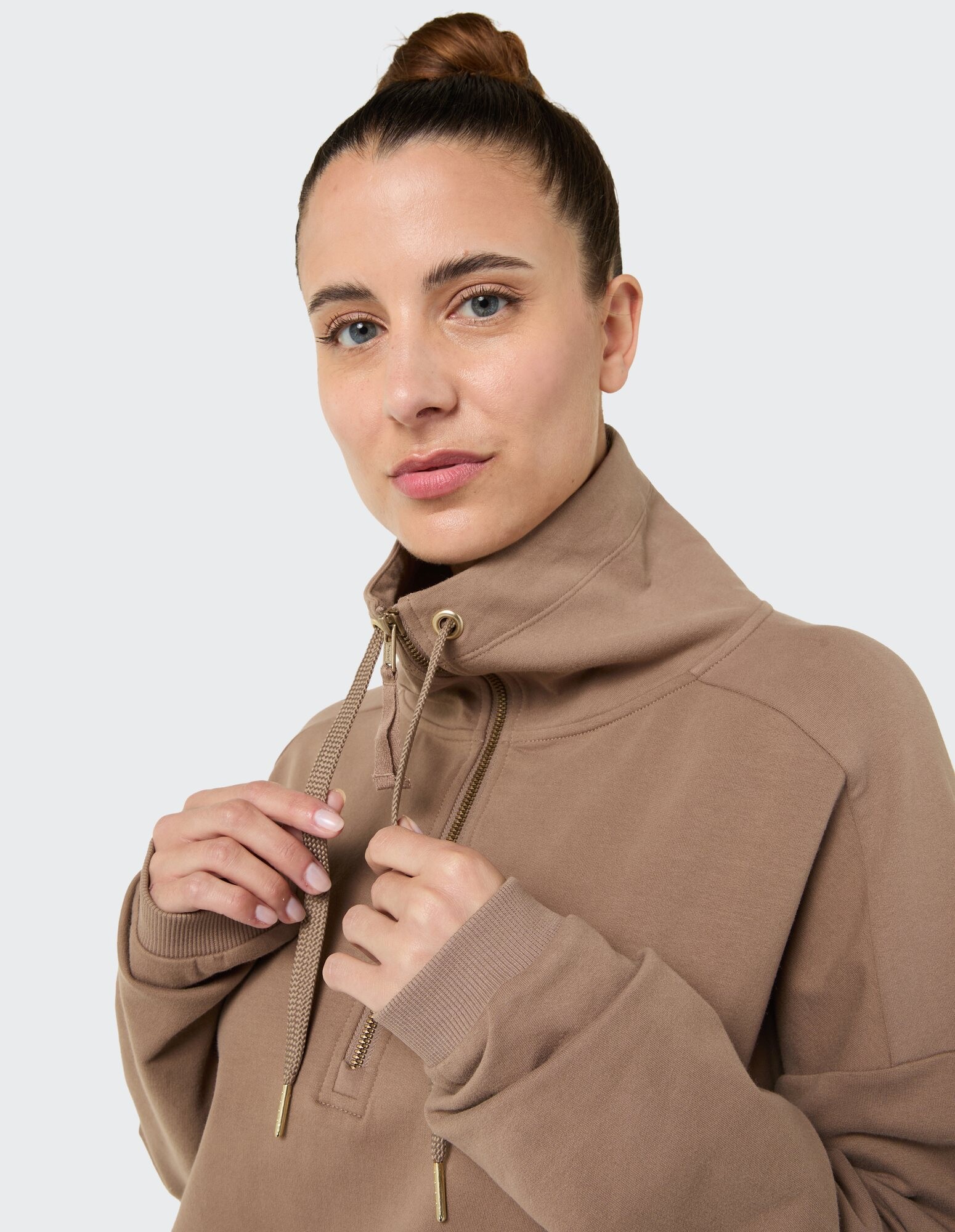 Nahaufnahme einer Frau in einem gemütlichen braunen Kapuzenpullover mit hohem Kragen und goldenen Akzenten.