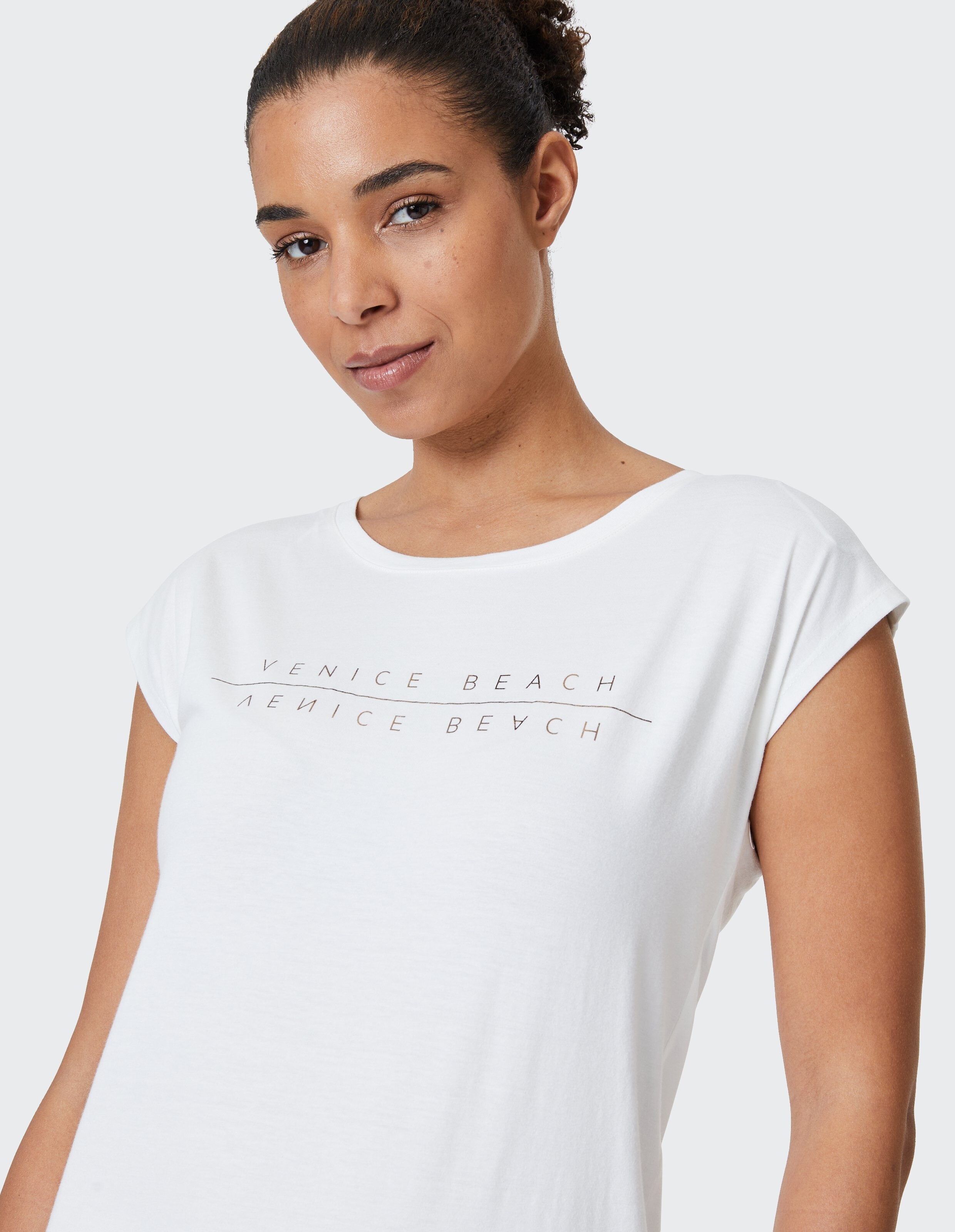 Frau trägt ein weißes Kurzarmhemd von Venice Beach Wonder für einen lässigen Stil.