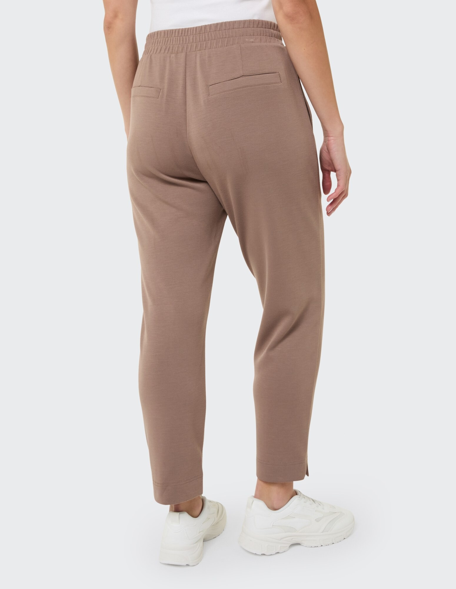 Rückansicht einer Frau in brauner Freizeithose mit elastischem Bund und Taschen.