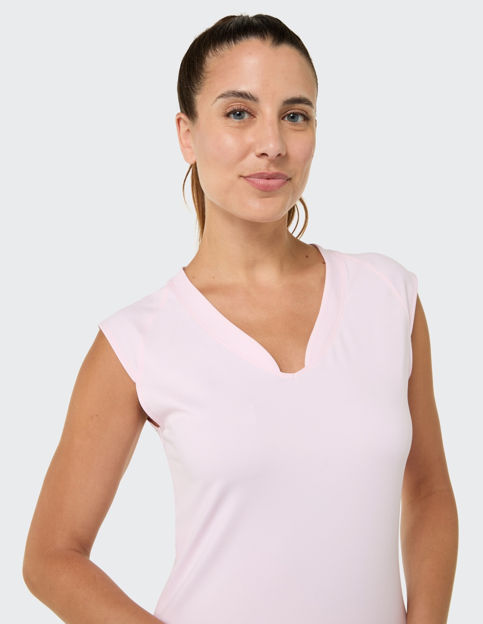 Frau in einem hellrosa ärmellosen Top mit V-Ausschnitt, das einen lässigen Stil unterstreicht.