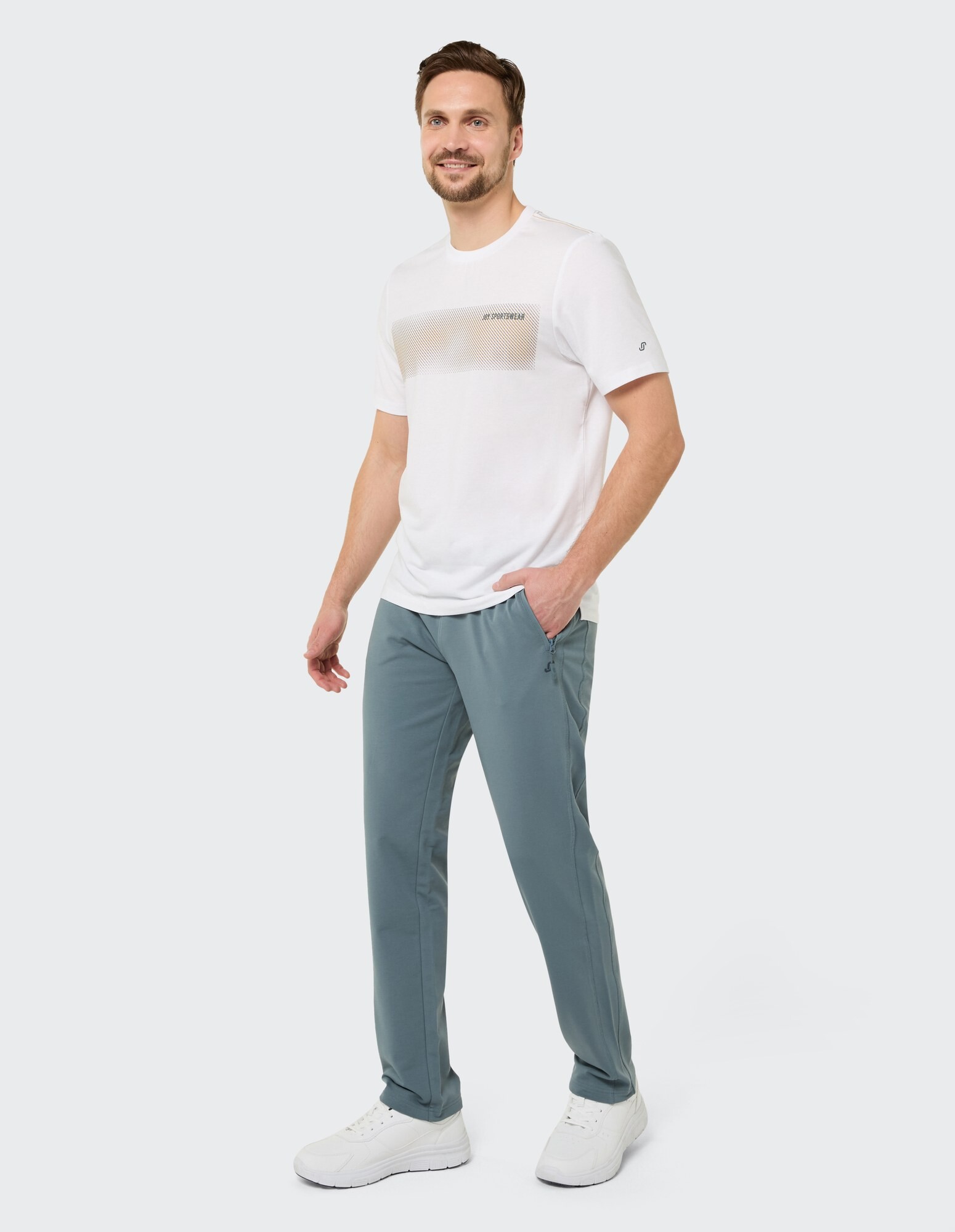 Mann trägt ein weißes T-Shirt und eine hellblaue Hose, lässig gestylt.
