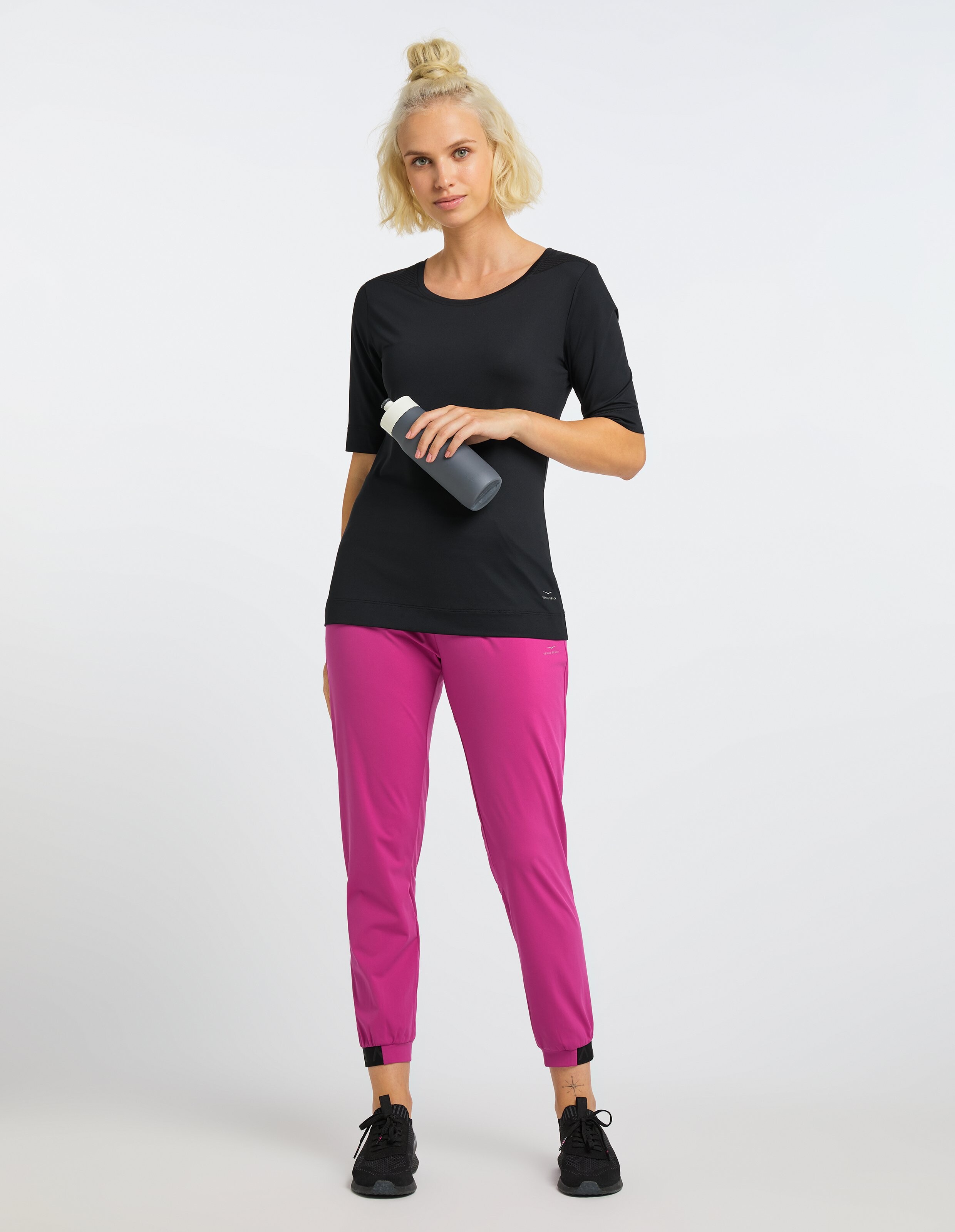 Frau trägt ein schwarzes Freizeithemd und rosa Jogginghosen, perfekt für einen bequemen Alltagsstil.