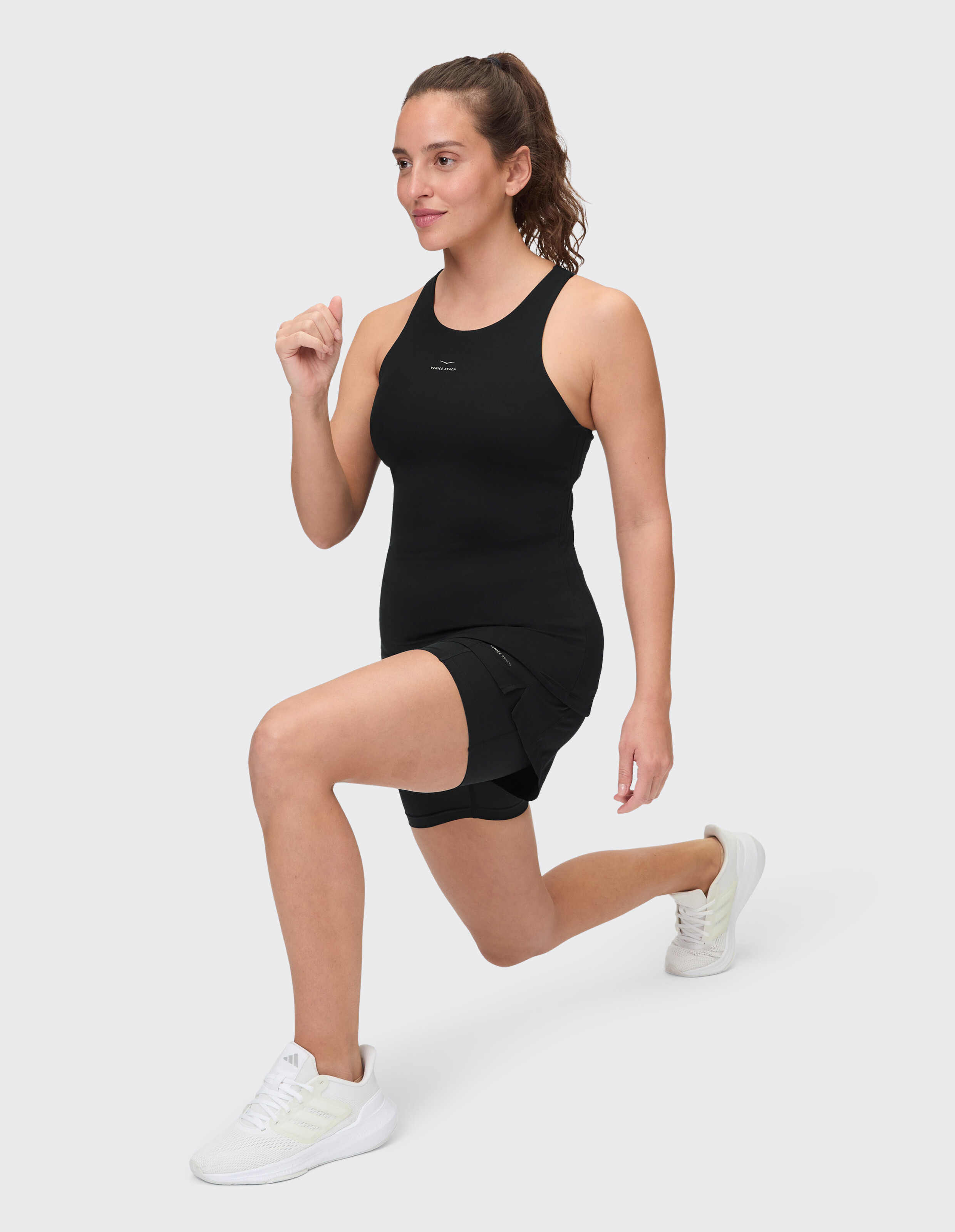 Frau in schwarzem Tanktop und Shorts macht einen Ausfallschritt, perfekt für aktive Freizeitkleidung.