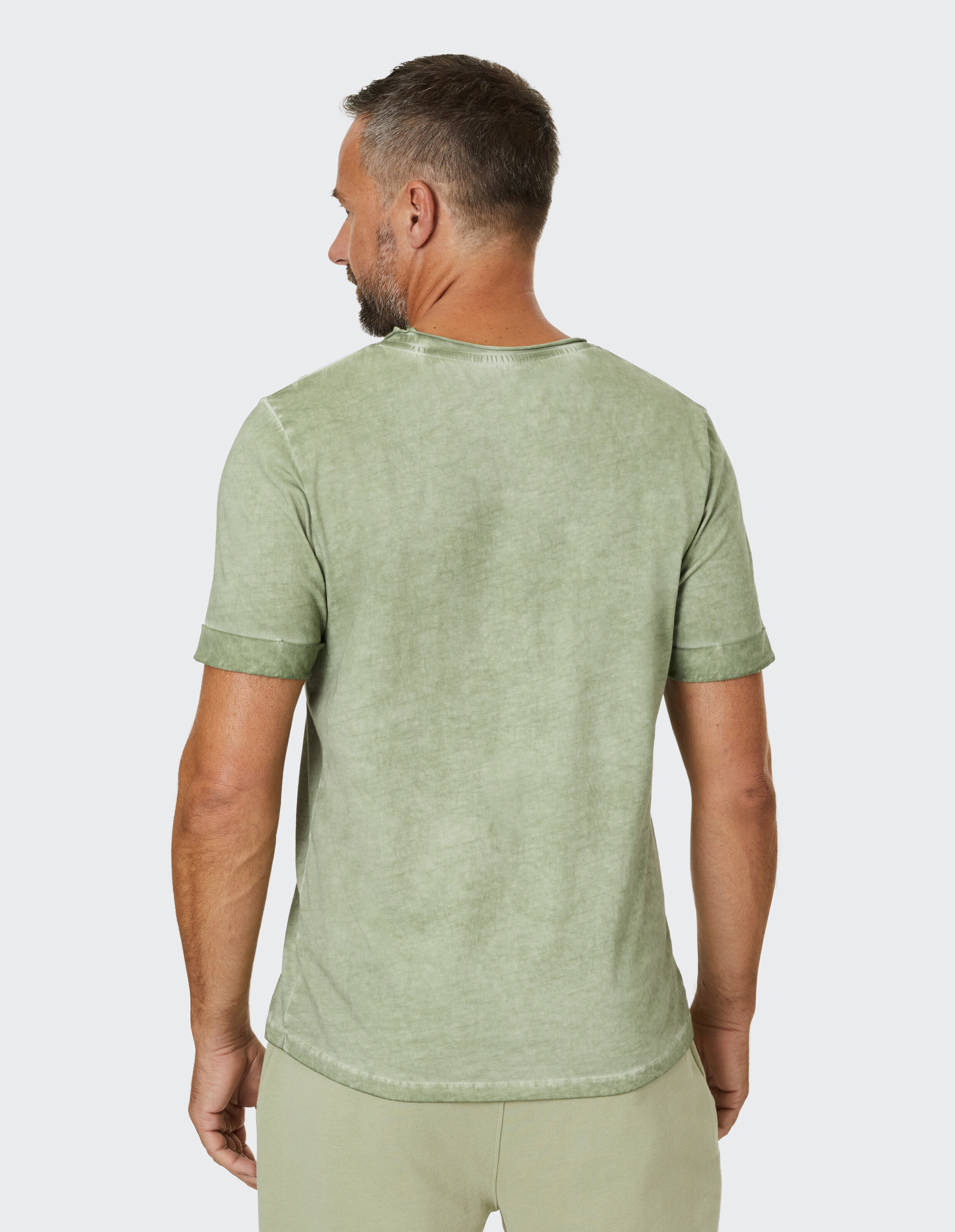 Rückansicht eines Mannes, der ein hellgrünes Freizeit-T-Shirt mit hochgekrempelten Ärmeln trägt.