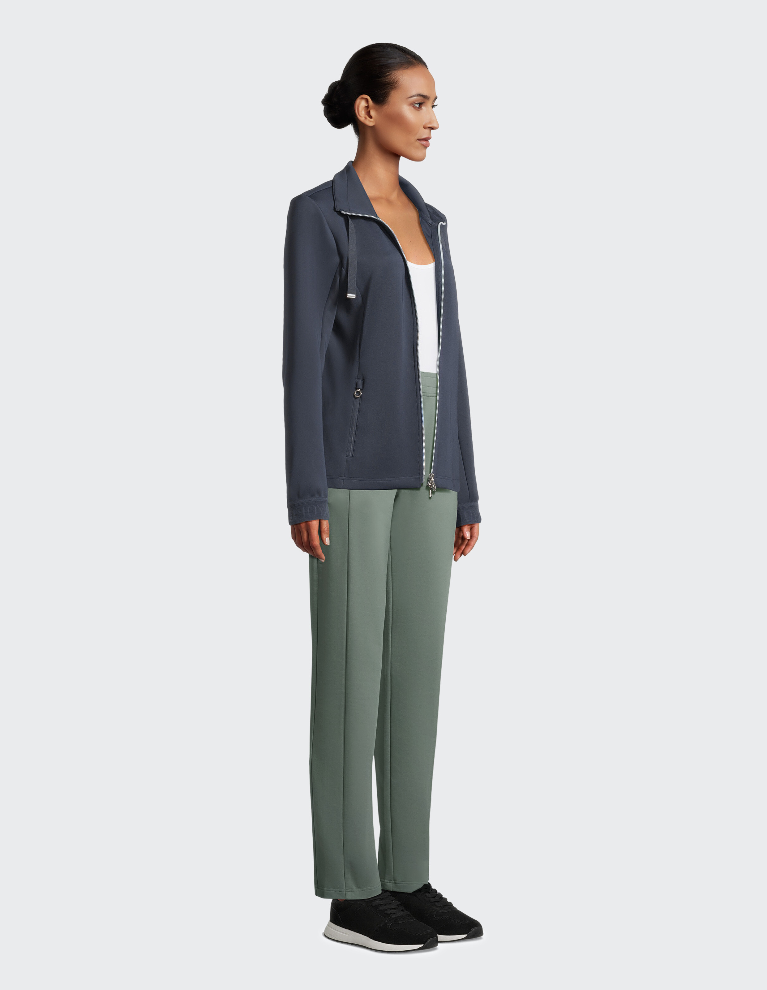 Das Model trägt eine dunkelblaue Jacke mit Reißverschluss und eine grüne, locker geschnittene Hose für Freizeitkleidung.