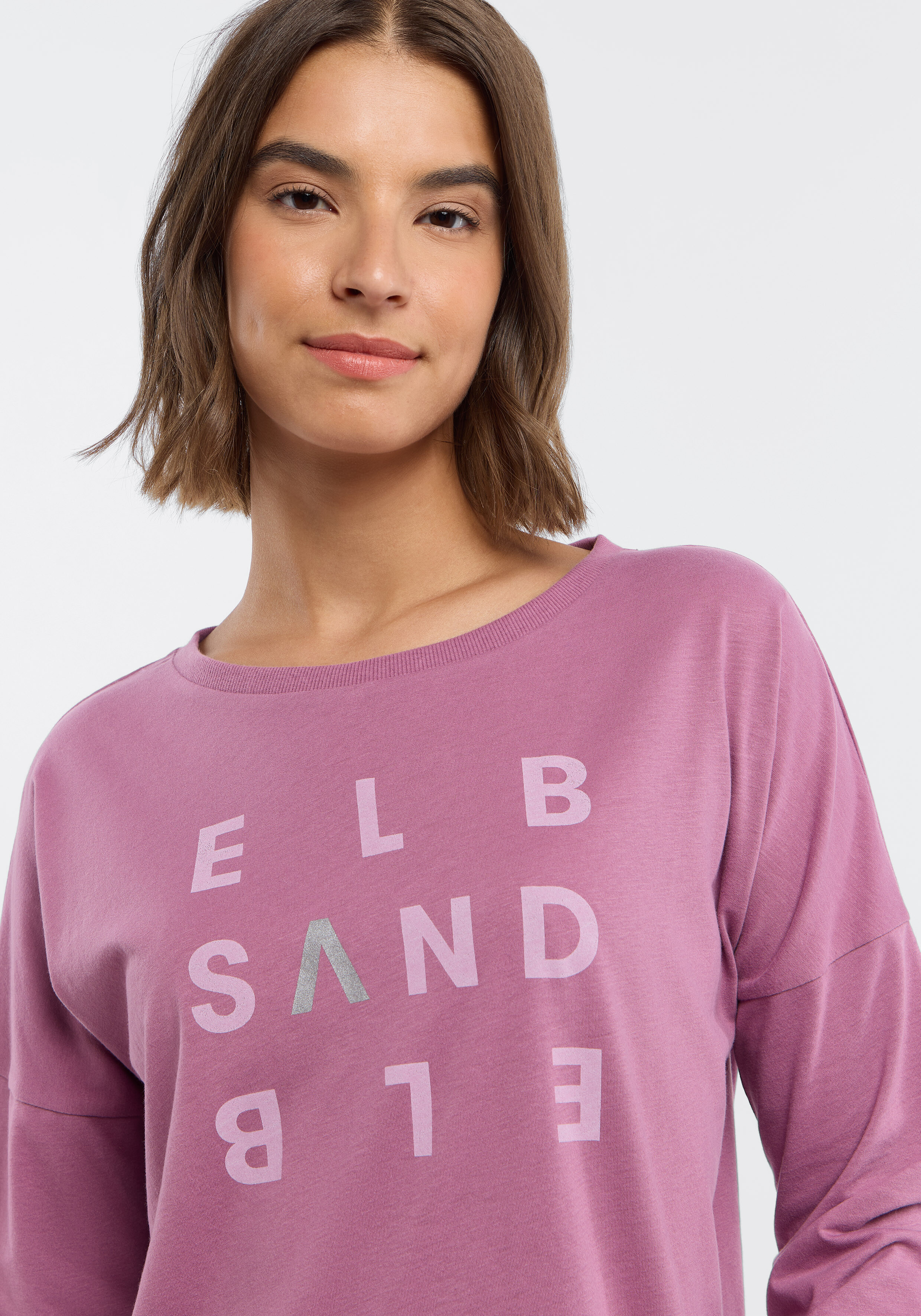 Frau trägt ein kuscheliges lila ELBSAND-Langarmshirt mit Logo-Print.