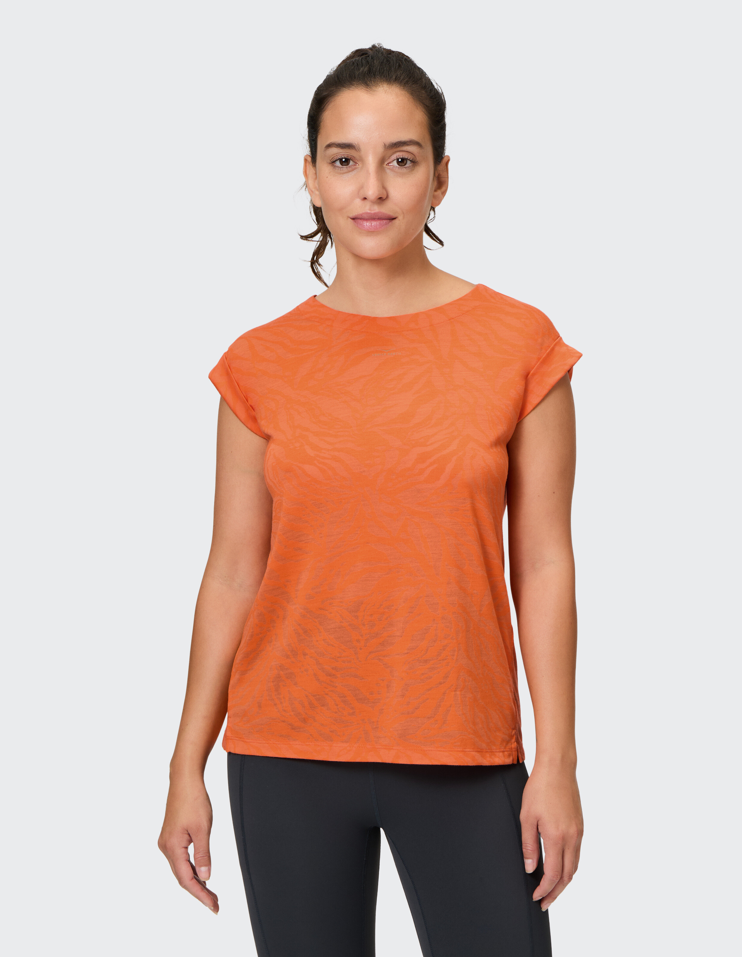 Frau trägt ein orange gemustertes Freizeit-T-Shirt mit aufgerollten Ärmeln.