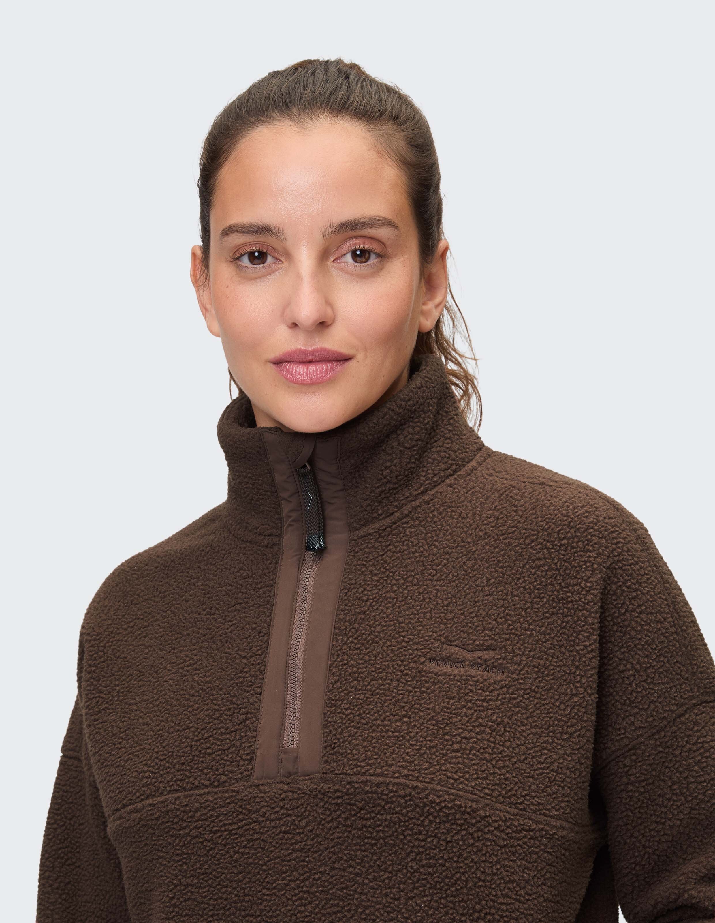Frau trägt ein braunes Fleece-Sweatshirt „Venice Beach Sarah“ mit halbem Reißverschluss.