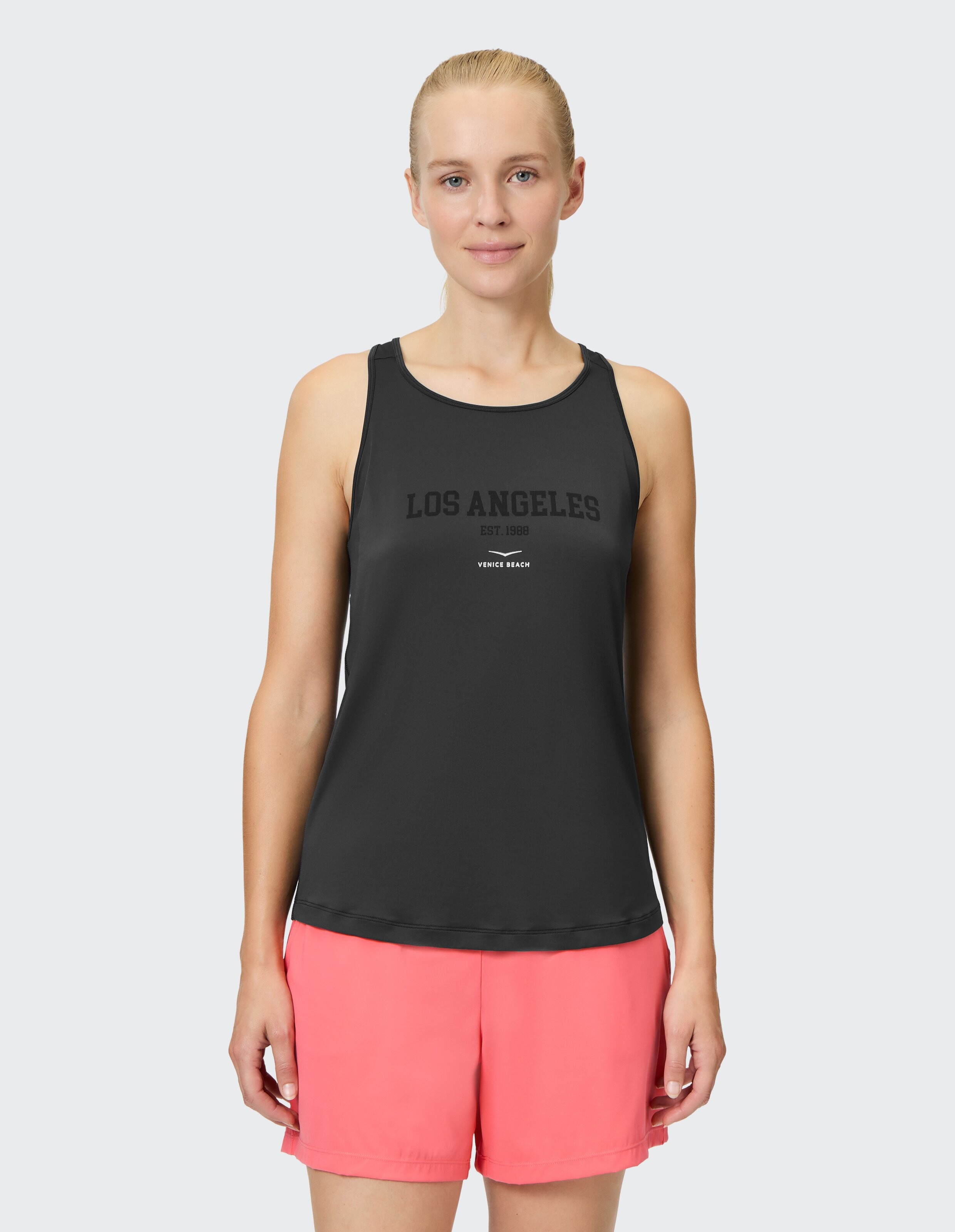 Frau trägt ein schwarzes Tanktop mit „Los Angeles“-Aufdruck und rosa Shorts.