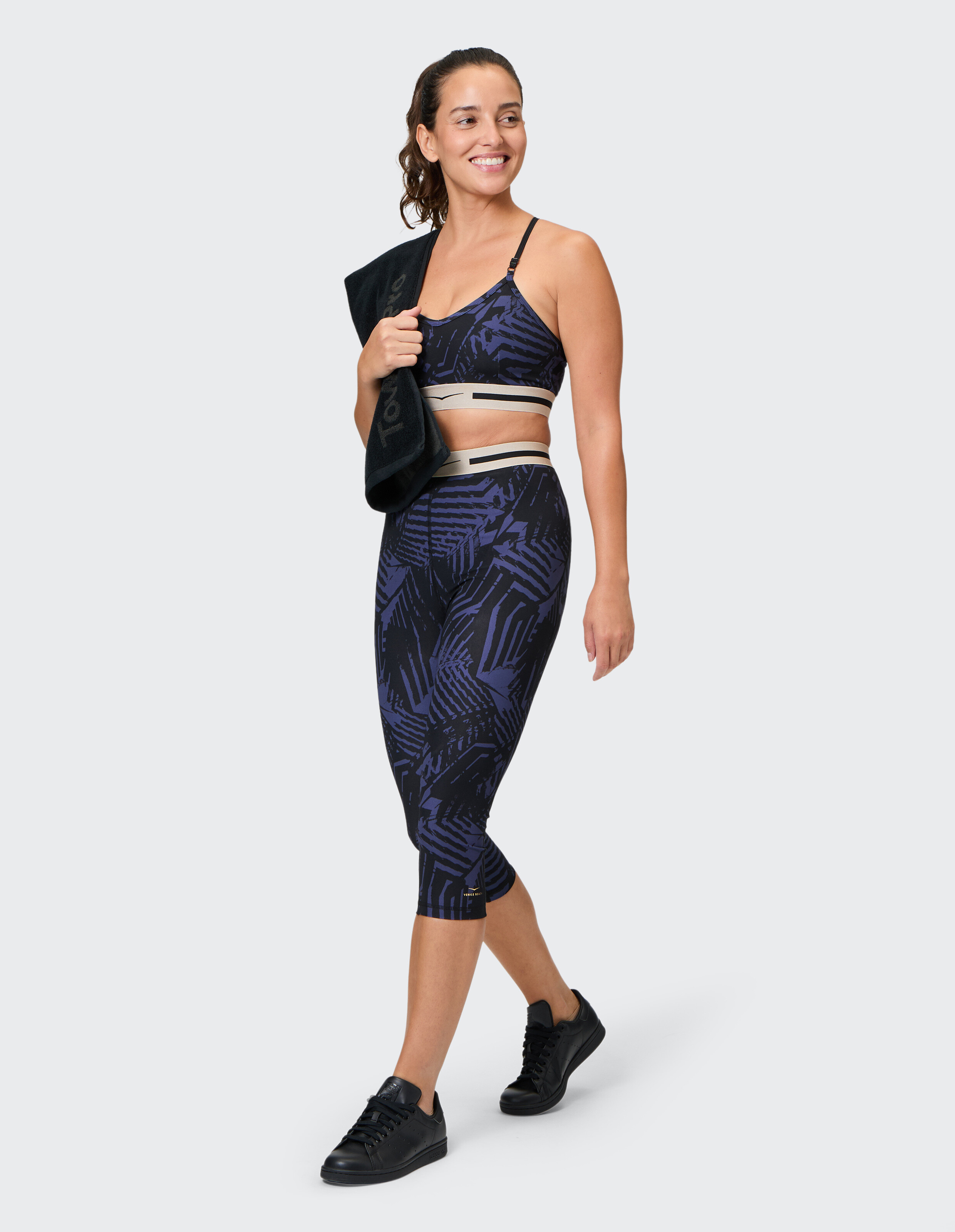 Frau trägt einen dunkelblauen gemusterten Sport-BH und Leggings im Set mit einem schwarzen Handtuch.