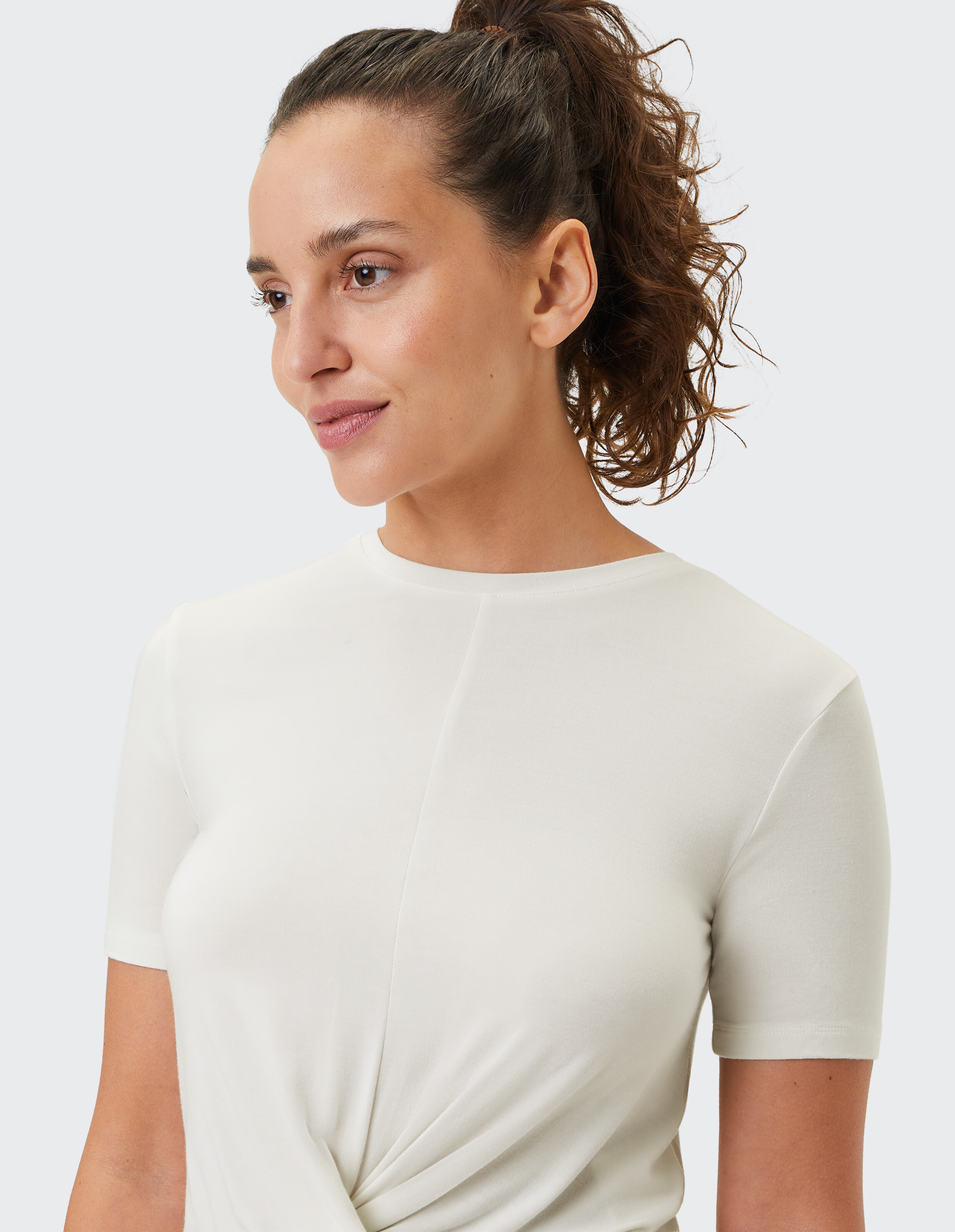 Nahaufnahme einer Frau, die ein cremefarbenes Kurzarm-Top mit Twist-Detail trägt.