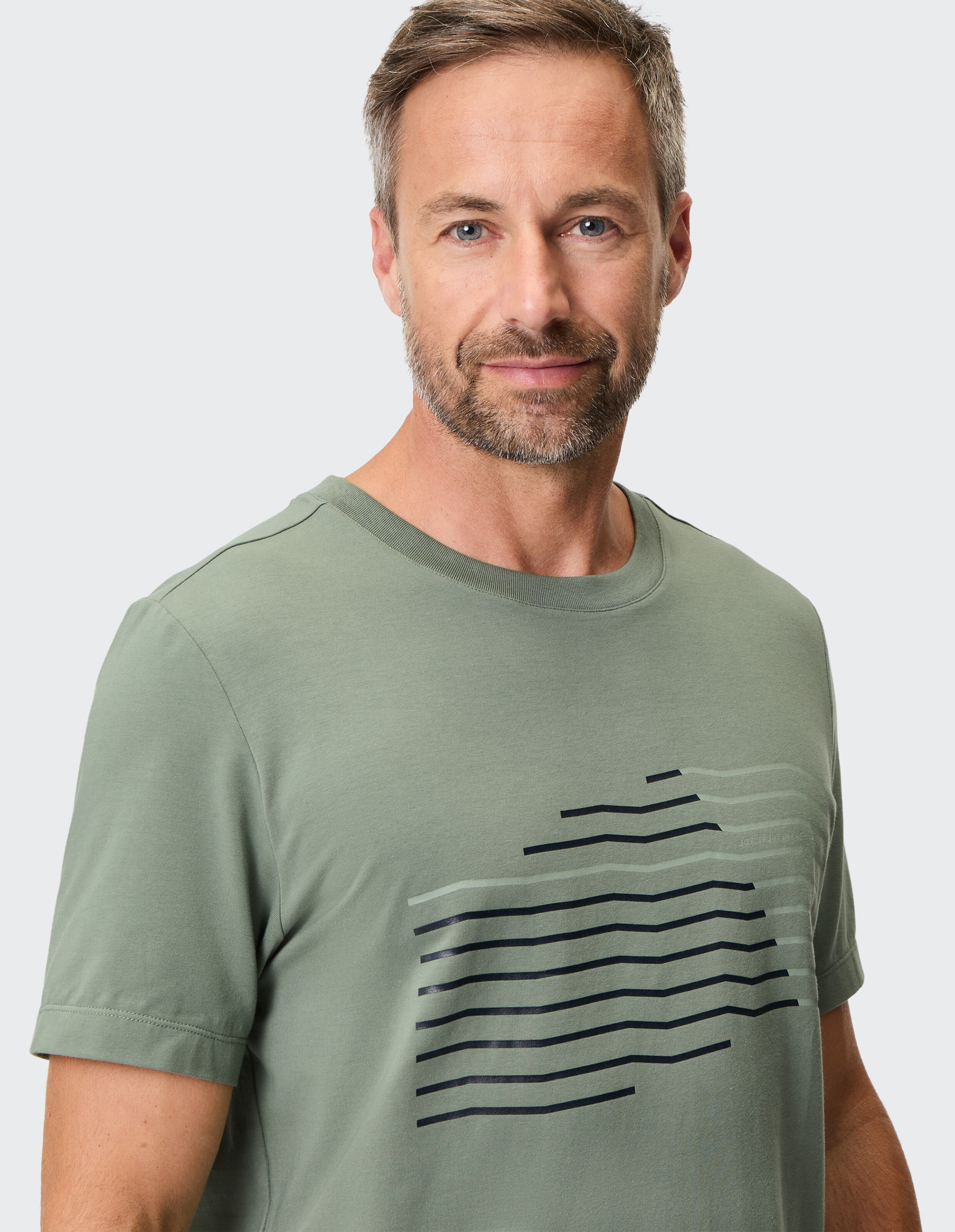 Mann trägt ein salbeigrünes Freizeit-T-Shirt mit einem modernen schwarzen Liniengrafikdruck.