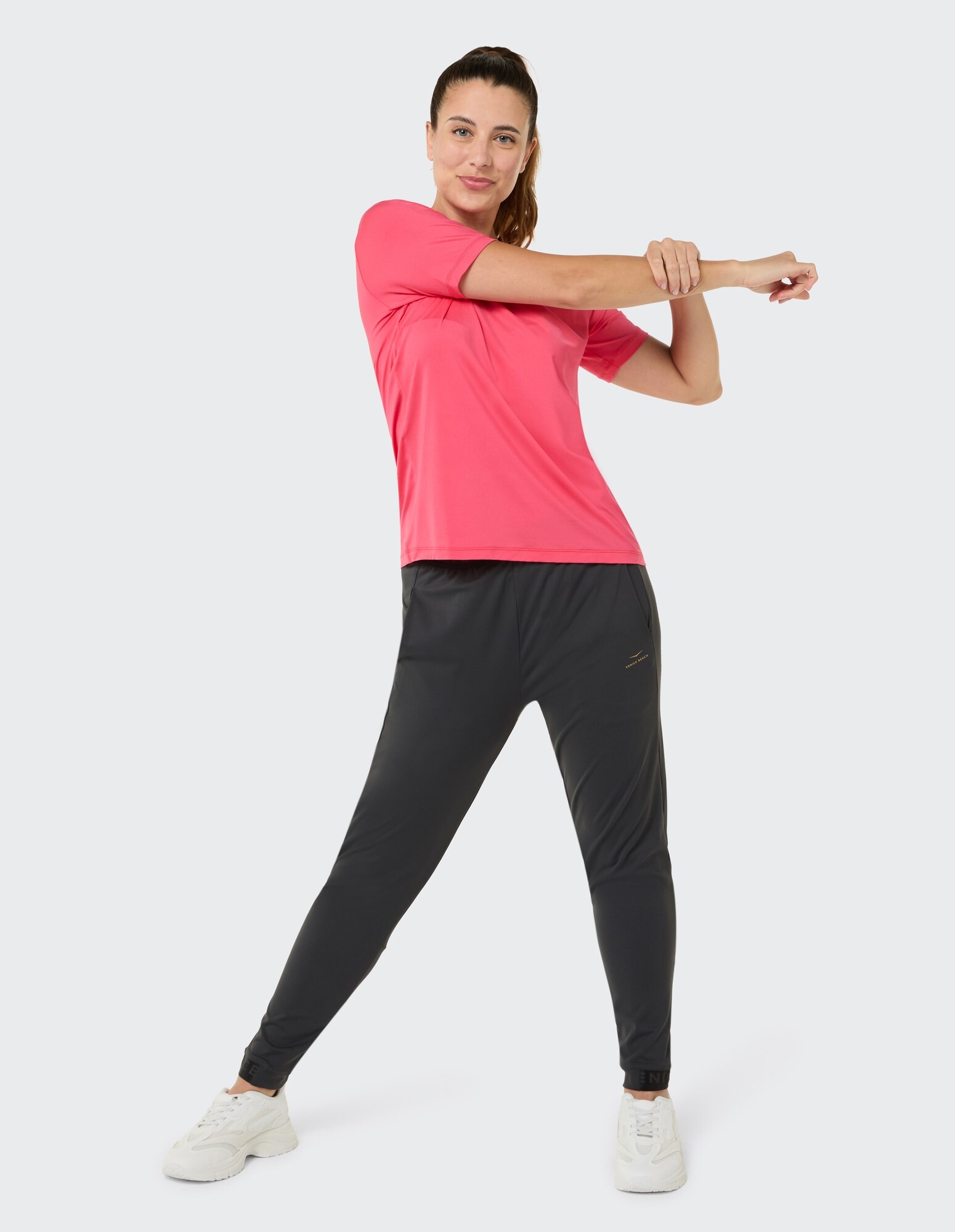 Frau beim Stretching in einem rosafarbenen Sportshirt und einer schwarzen Jogginghose, perfekt für Freizeitkleidung.