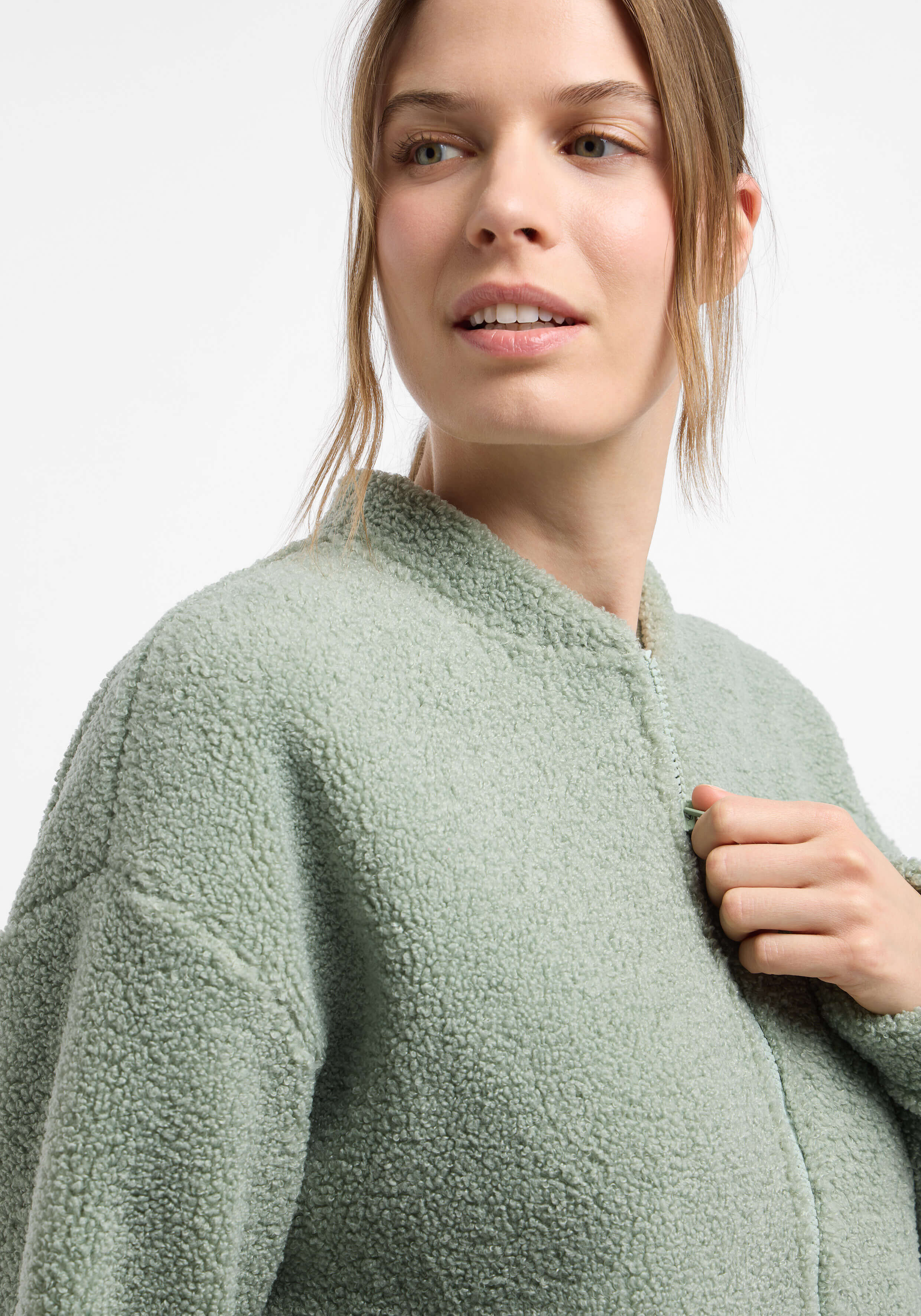 Frau trägt eine kuschelige, salbeigrüne Teddyfleece-Reißverschlussjacke für lässige Loungewear.
