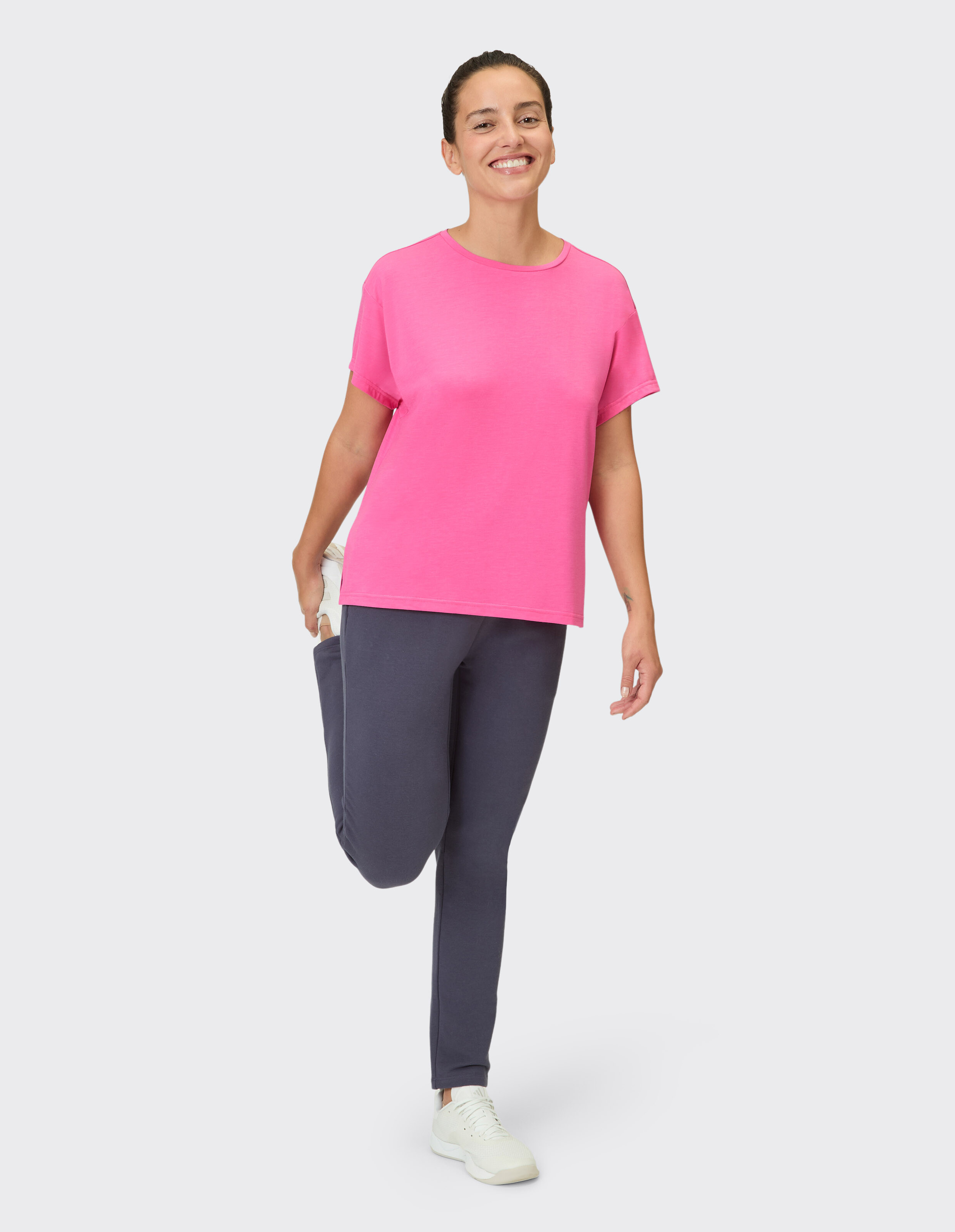 Frau in einem leuchtend rosa T-Shirt und dunklen Leggings lächelt und posiert lässig.