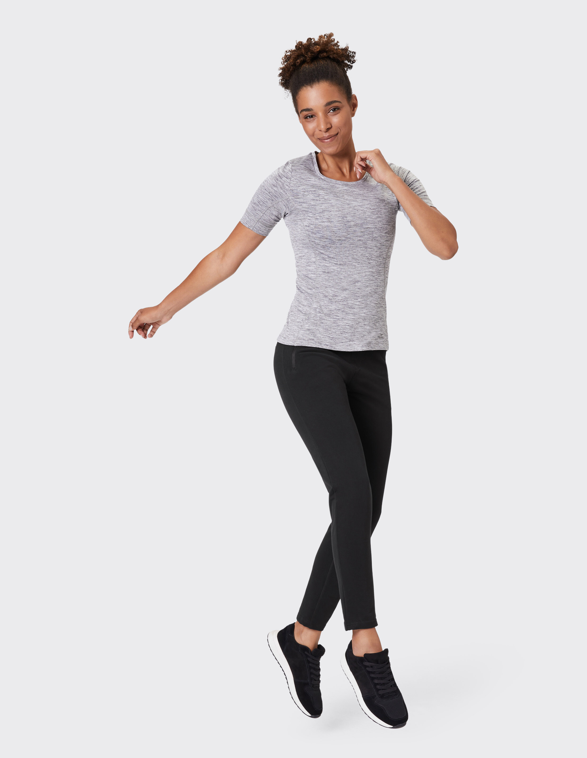 Frau in einem grauen T-Shirt und einer schwarzen Hose, die einen lässigen, sportlichen Stil zeigt.