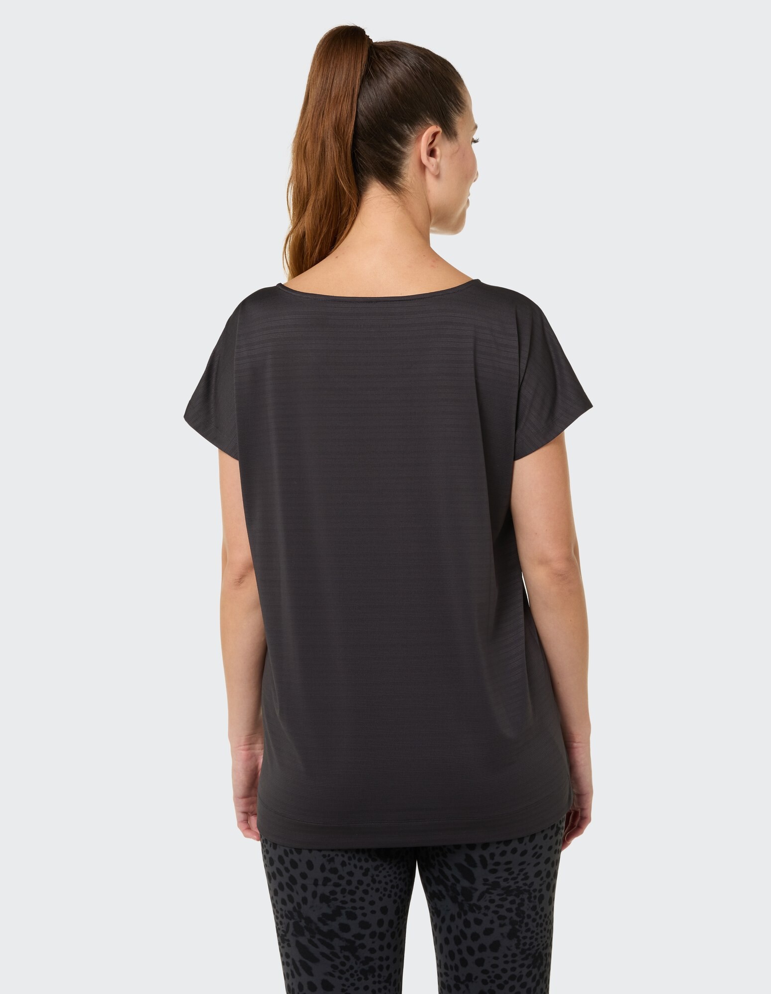 Rückansicht einer Frau in einem locker sitzenden schwarzen Top und gemusterten Leggings.