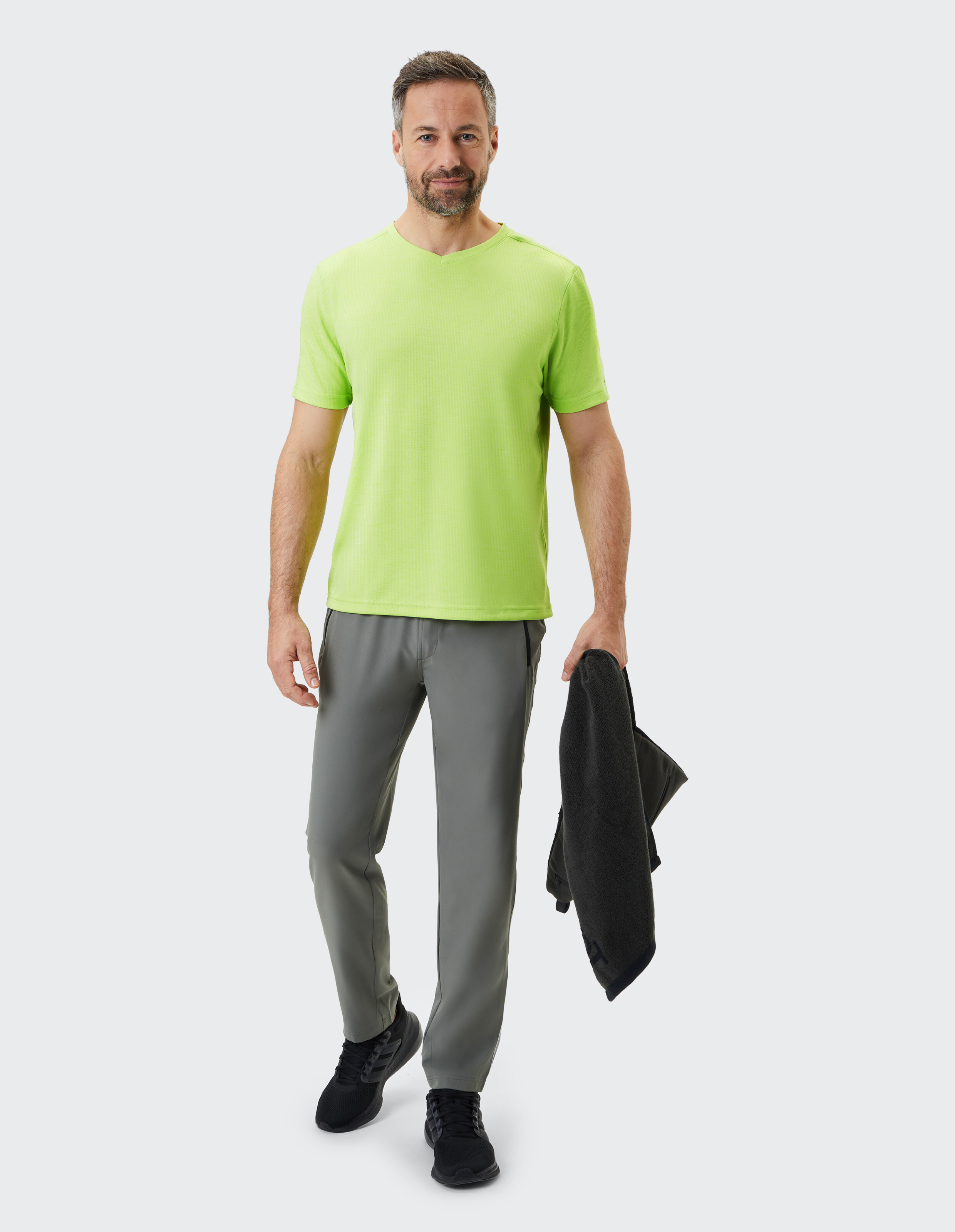 Mann in hellgrünem T-Shirt und grauer Hose, Jacke in der Hand, lässiger Stil.