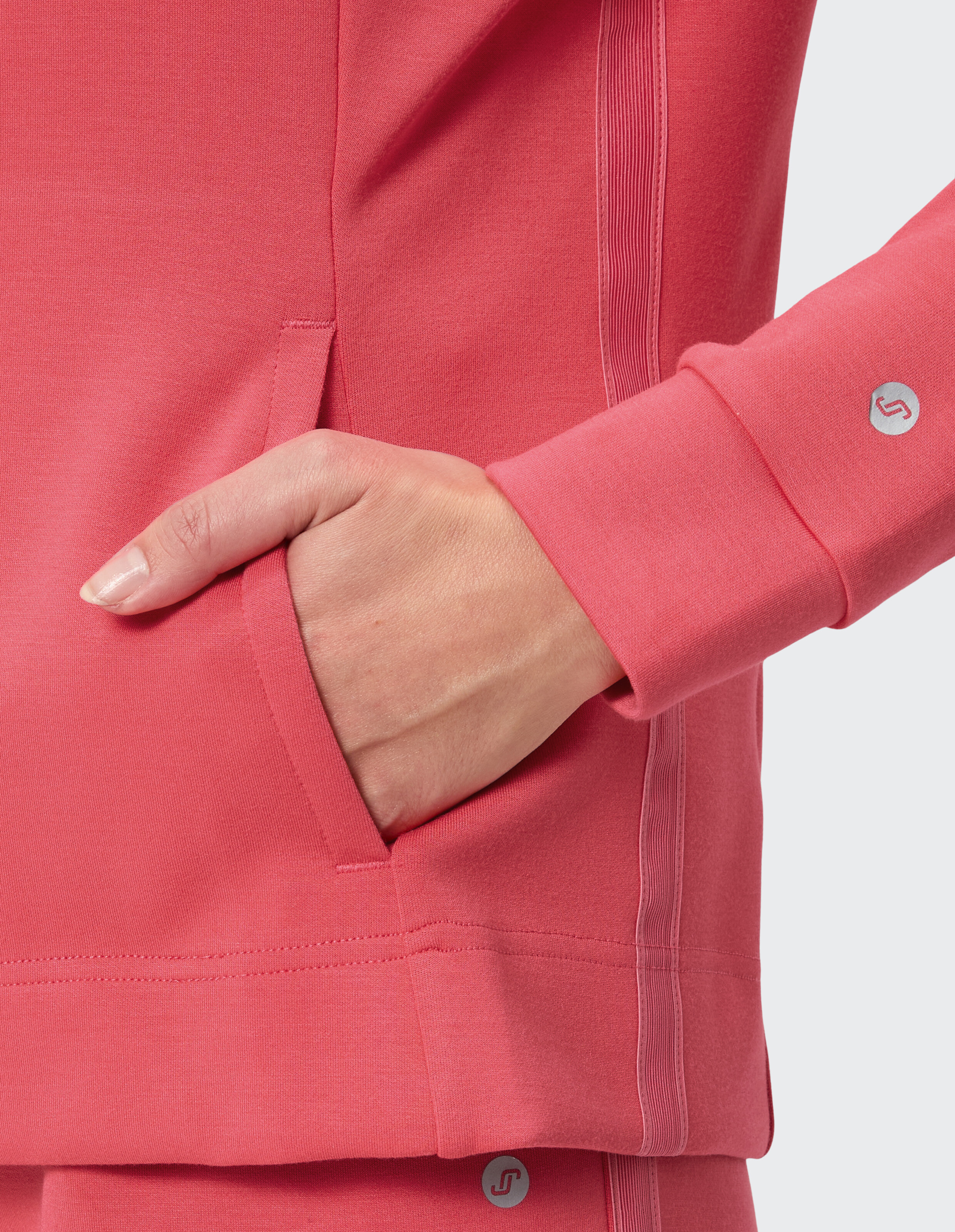 Nahaufnahme der Hand einer Frau in einem rosa Freizeitoberteil mit Tasche, das weiches Material und stilvolles Design zur Schau stellt.