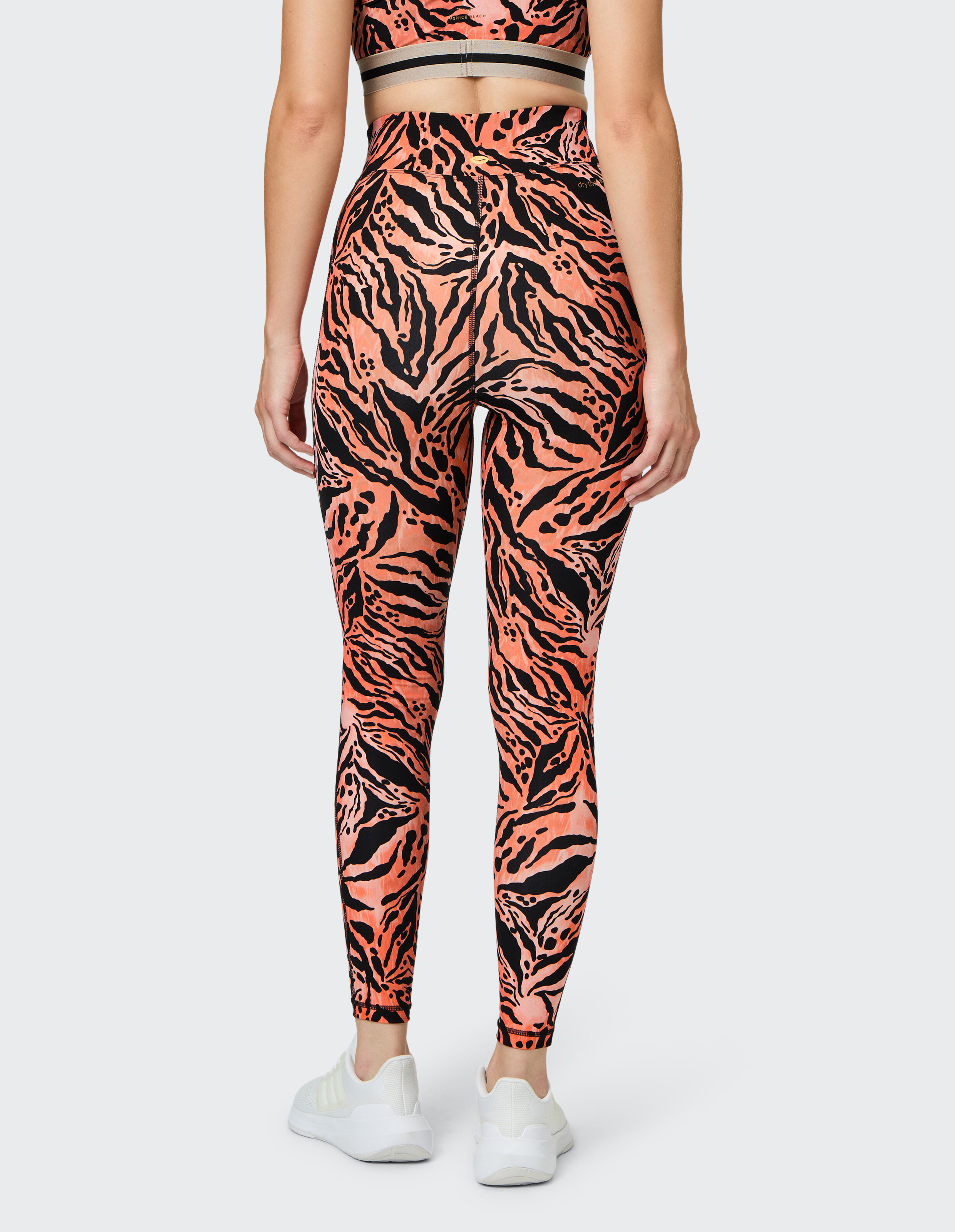 Rückansicht einer Frau, die leuchtend orangefarbene und schwarze Leggings mit Tigermuster trägt, gepaart mit weißen Turnschuhen.