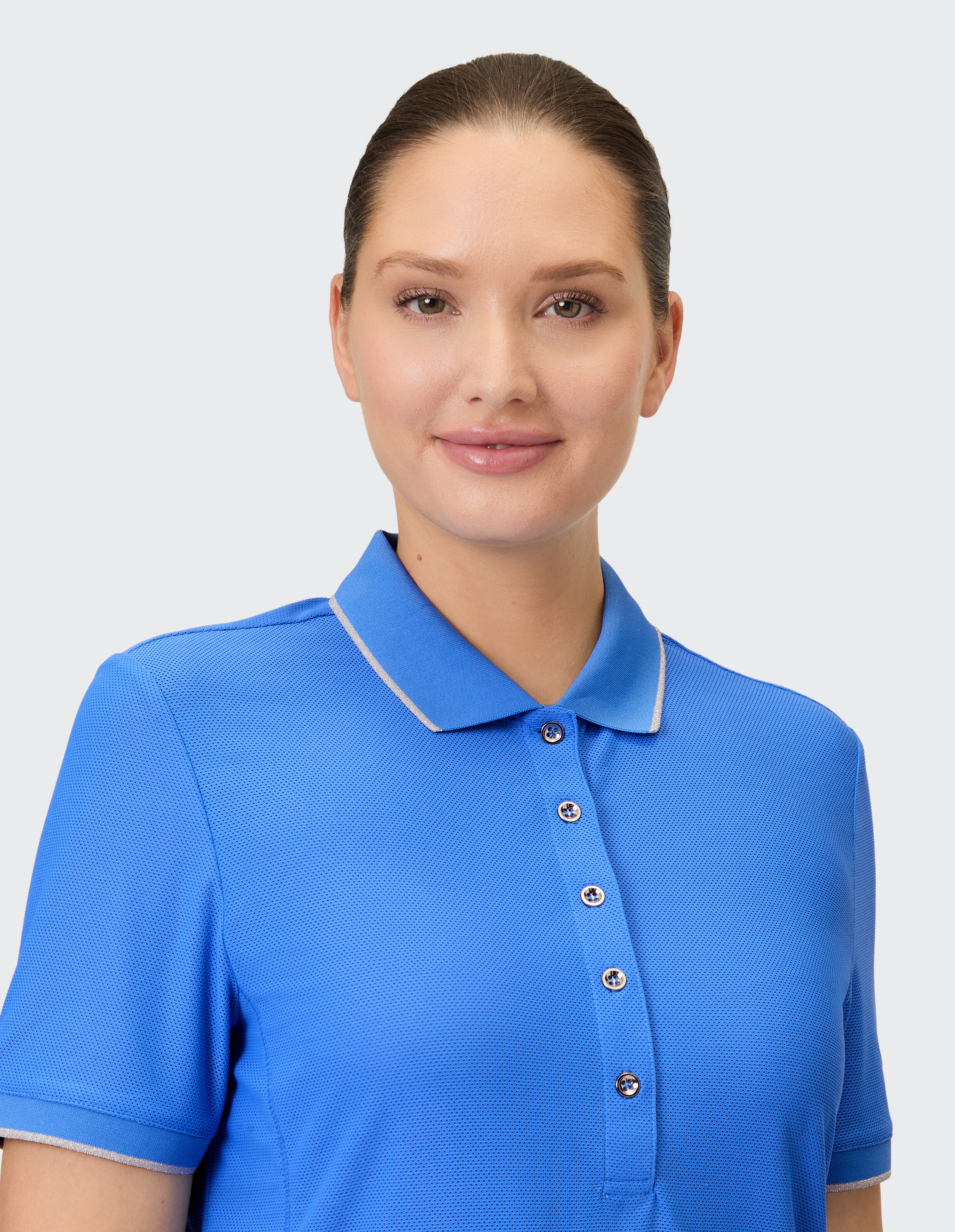 Eine Frau trägt ein blaues Poloshirt mit silbernen Akzenten am Kragen und an den Ärmelbündchen.