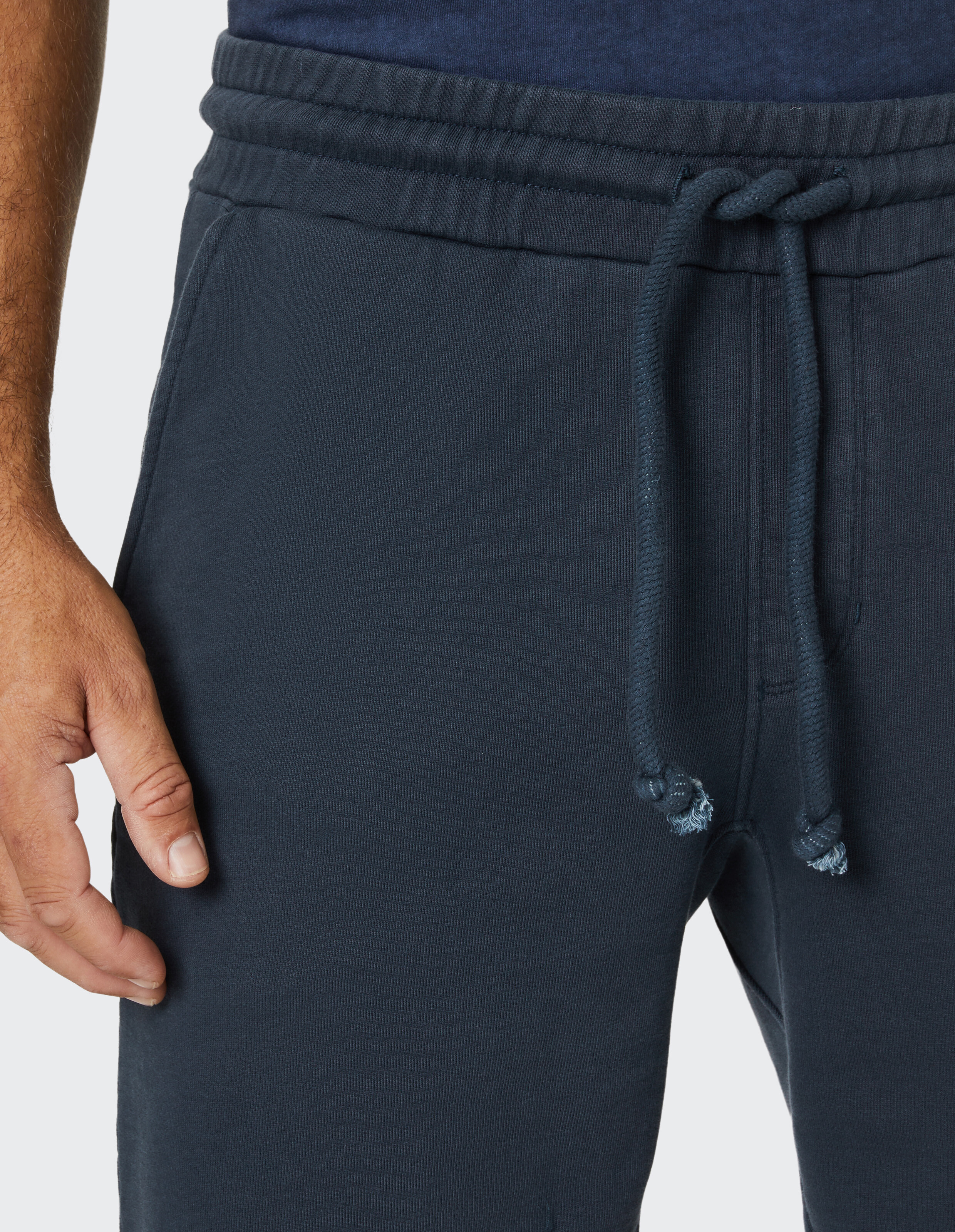Nahaufnahme einer dunkelblauen Jogginghose mit Kordelzug um die Taille, daneben eine Hand in entspanntem Zustand.