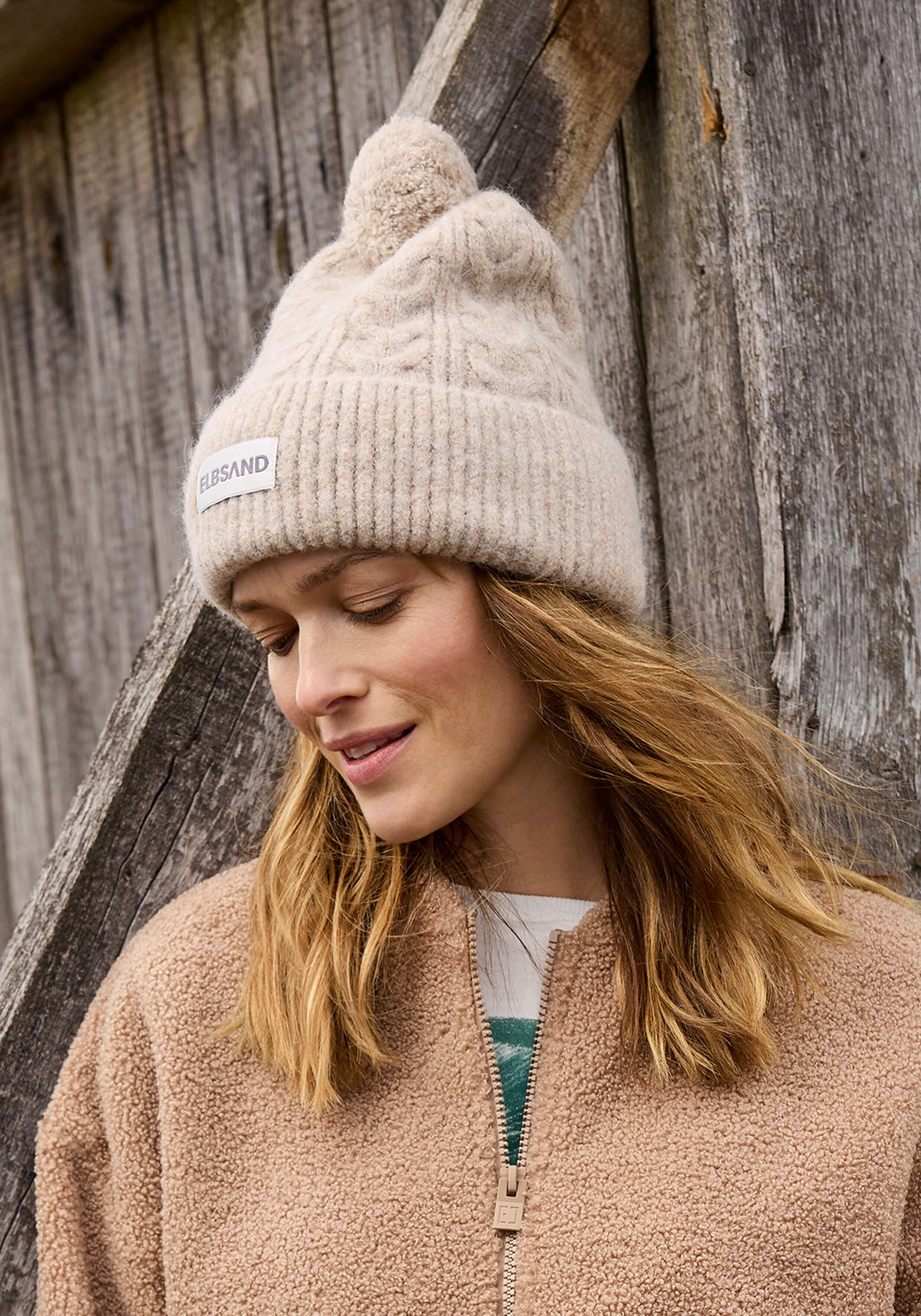Kuschelige beige Strickmütze mit Bommel, gepaart mit einer weichen braunen Fleecejacke.