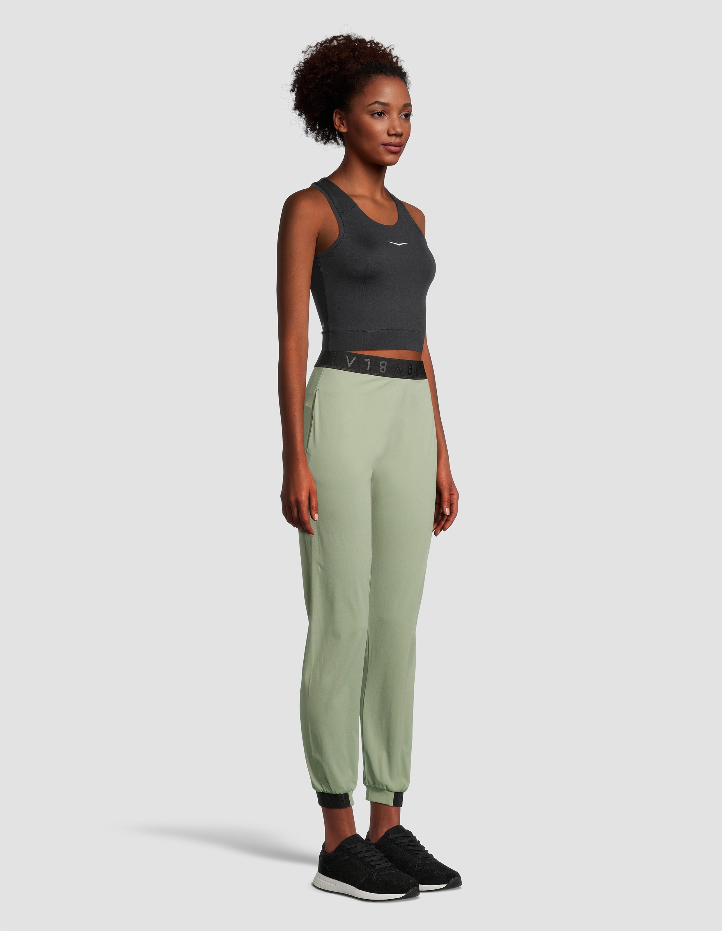 Frau trägt ein dunkelgraues Crop-Top und hellgrüne Freizeit-Jogginghosen für Aktivkleidung.